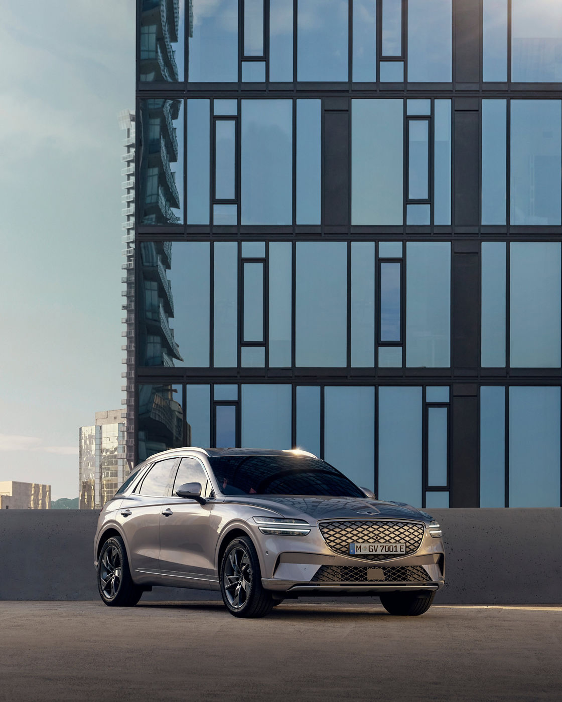 Genesis GV70 in grey outdoors in front of a glass house wall