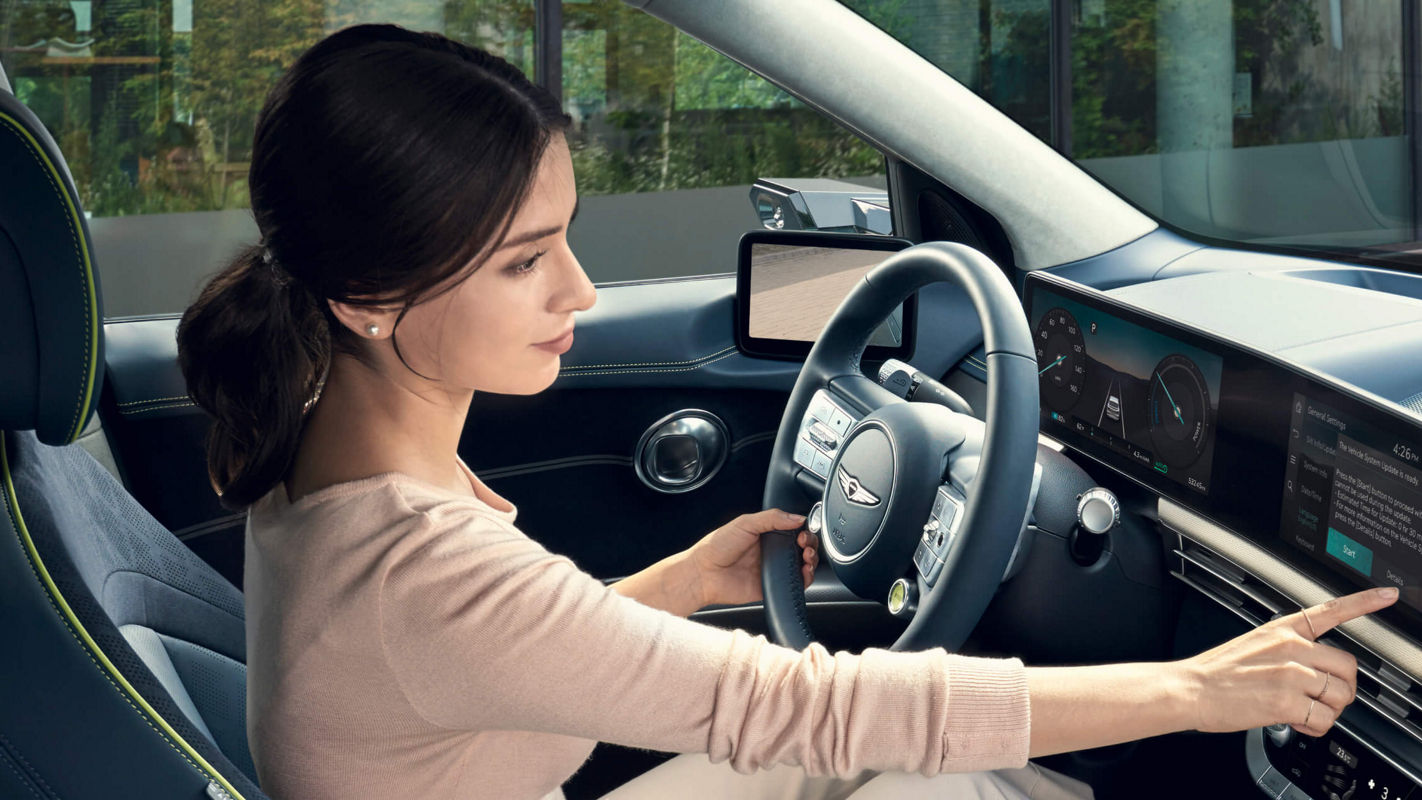 Woman in the driver's seat of the Genesis GV60, operating the display above the centre console