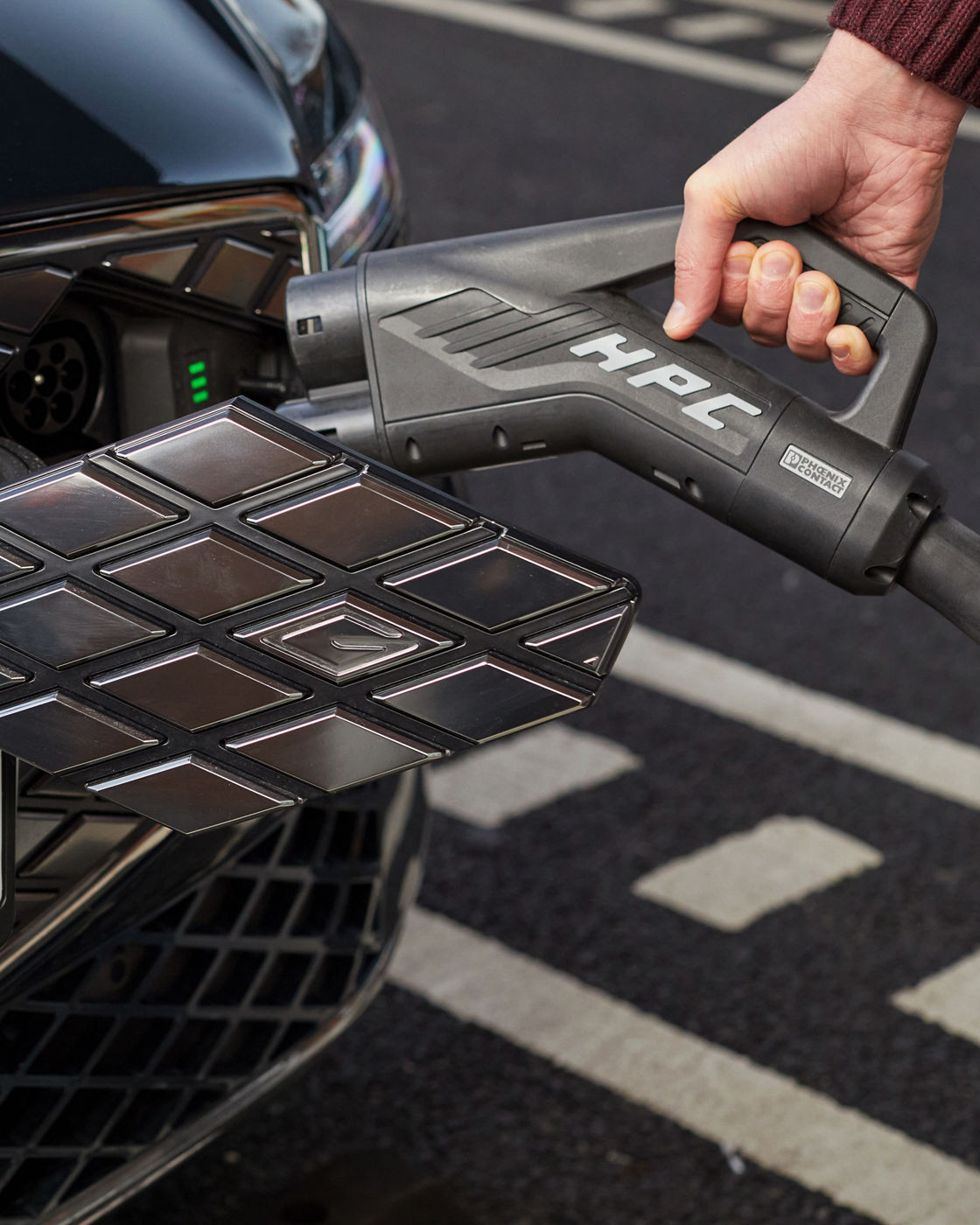 A hand plugs a charging cable into an electric car