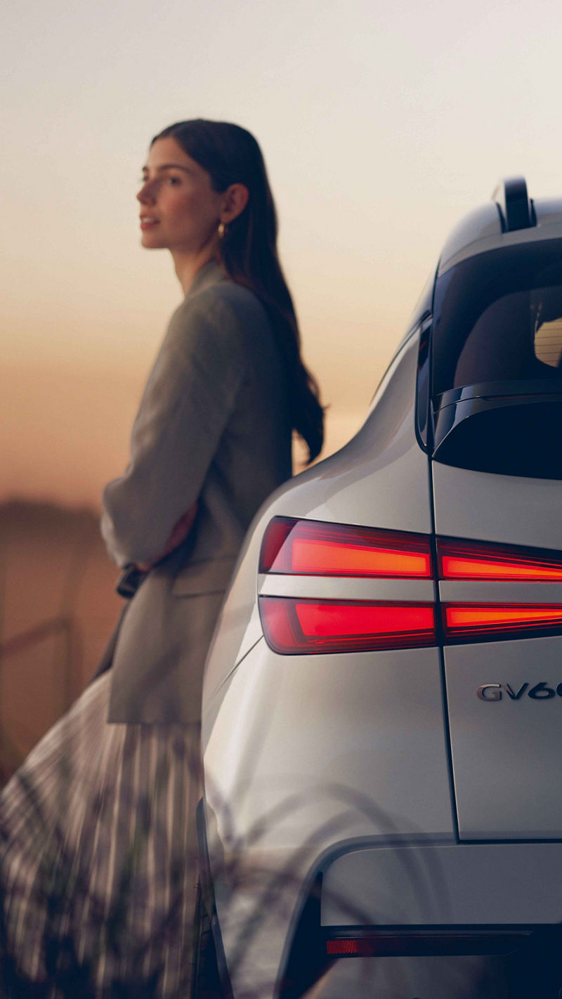 Woman leaning against a Genesis GV60 and looking into the distance