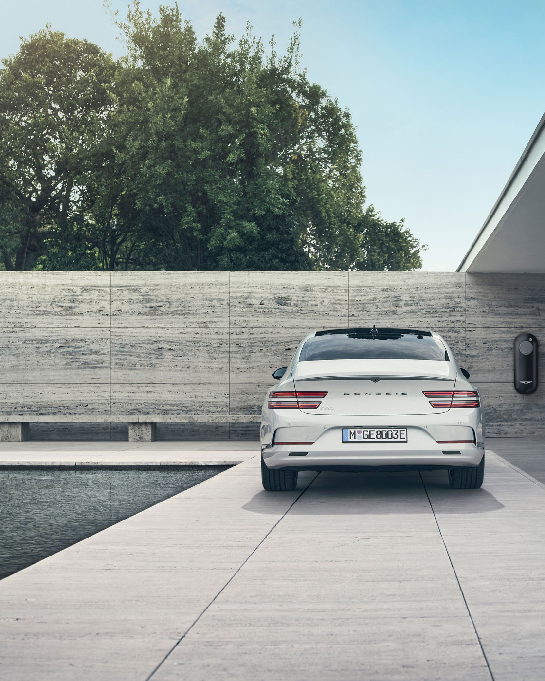 White Genesis eG80 in front of house with pool and next to a charging station - rear view