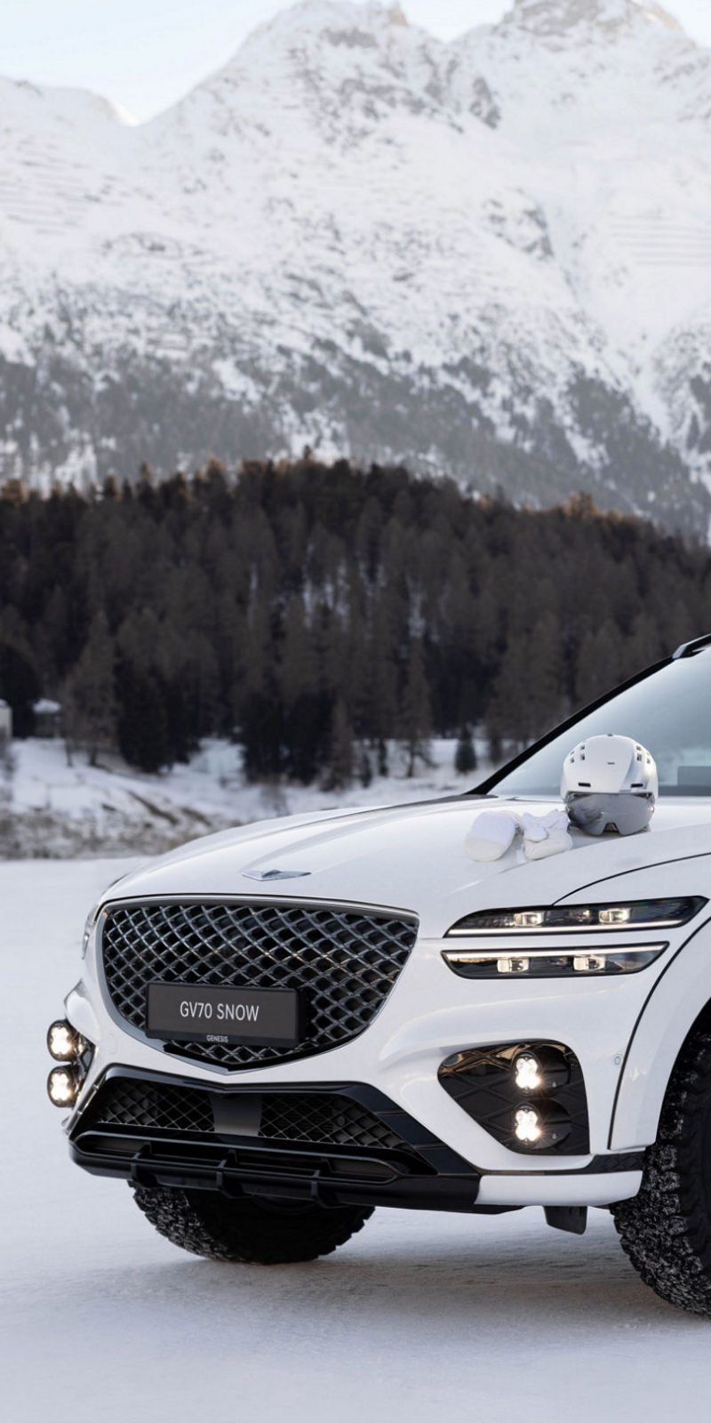 White Genesis G70 Snow concept on snow with ski equipment in front of snow-covered mountains