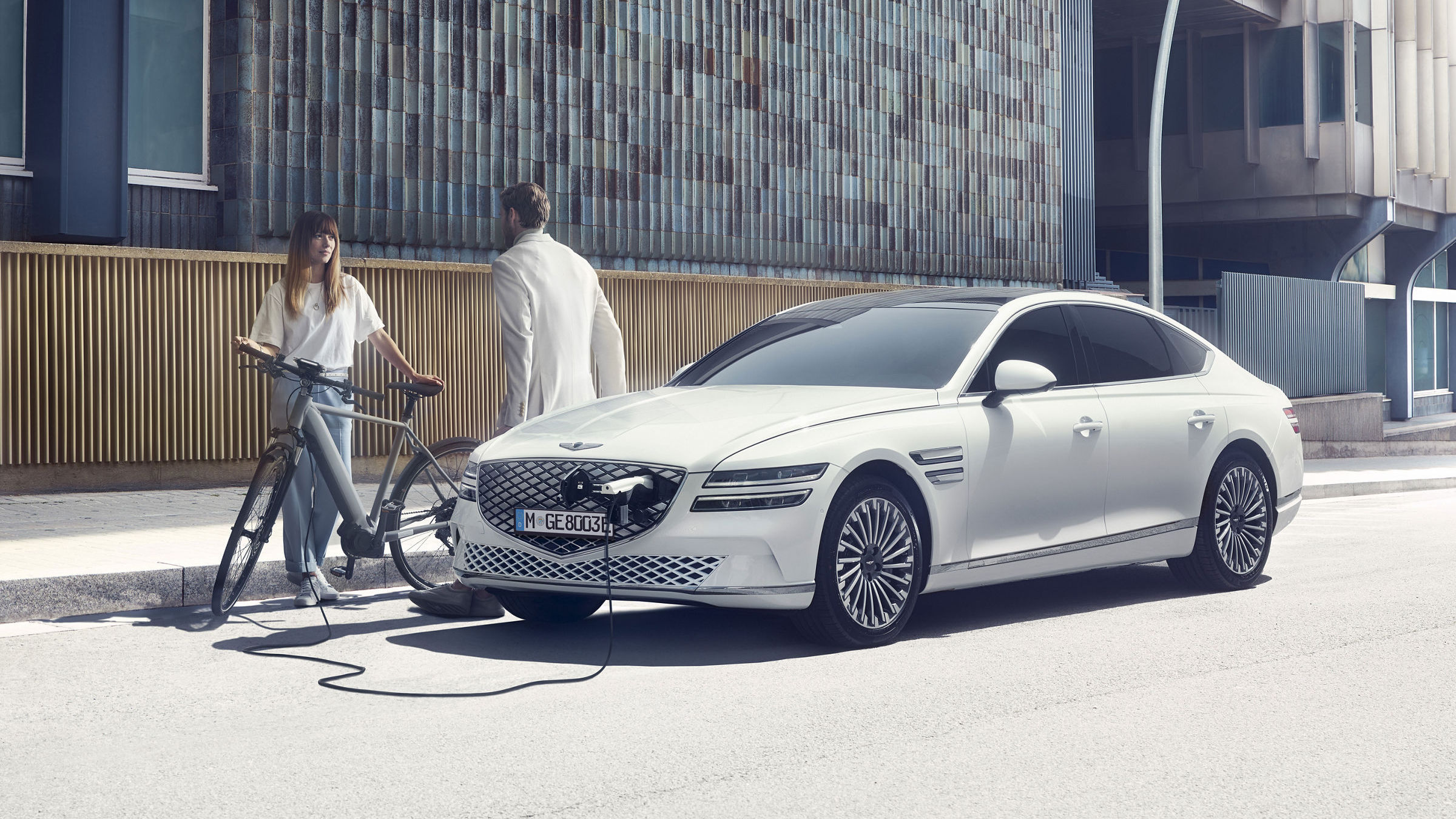 White Genesis eG80 charging on the street in the city, two people chatting.