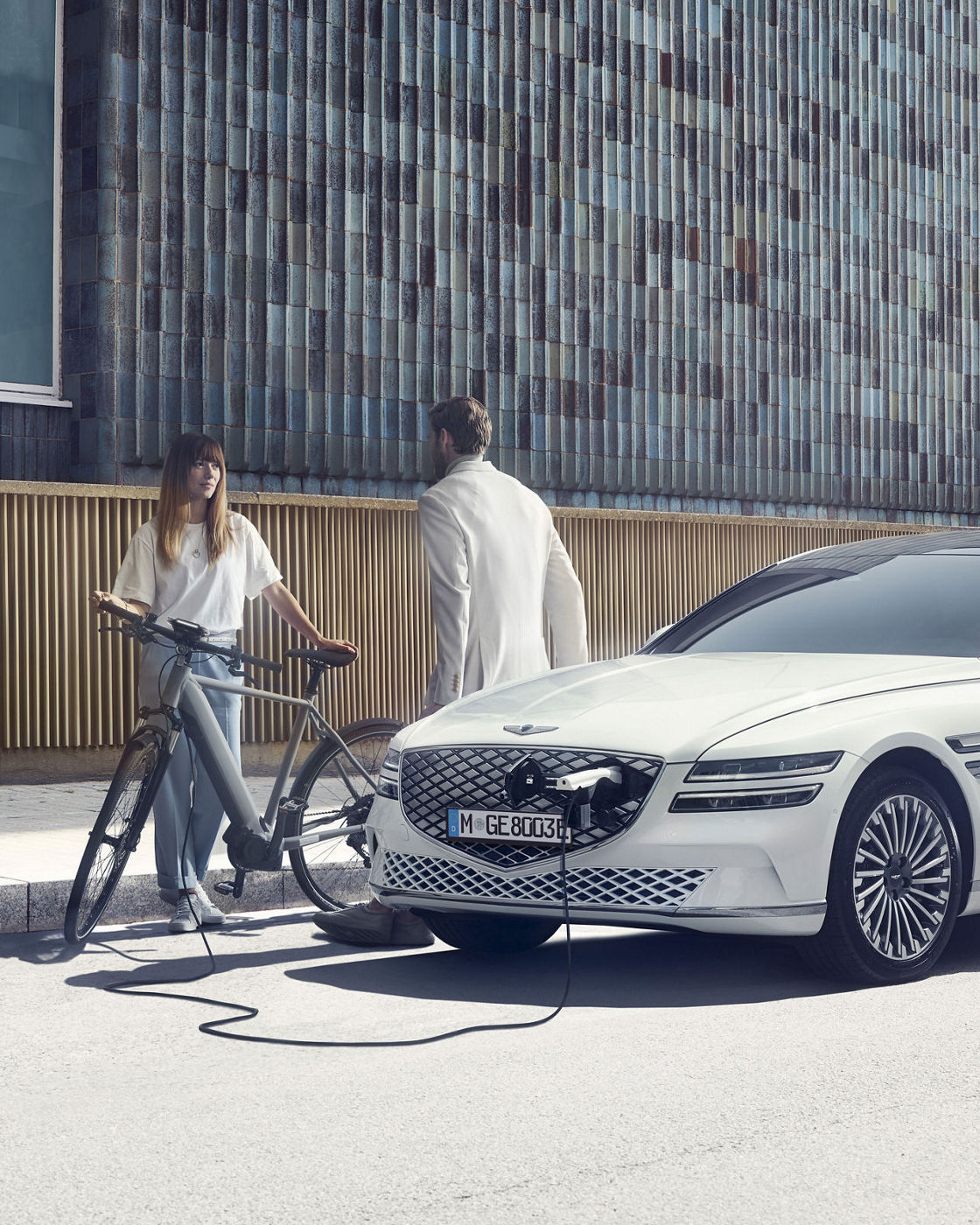 White Genesis eG80 charging on the street in the city, two people chatting.