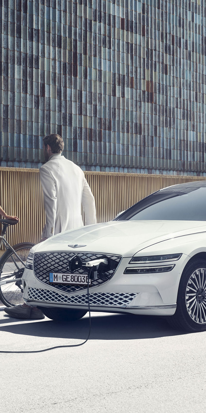 White Genesis eG80 charging on the street in the city, two people chatting.