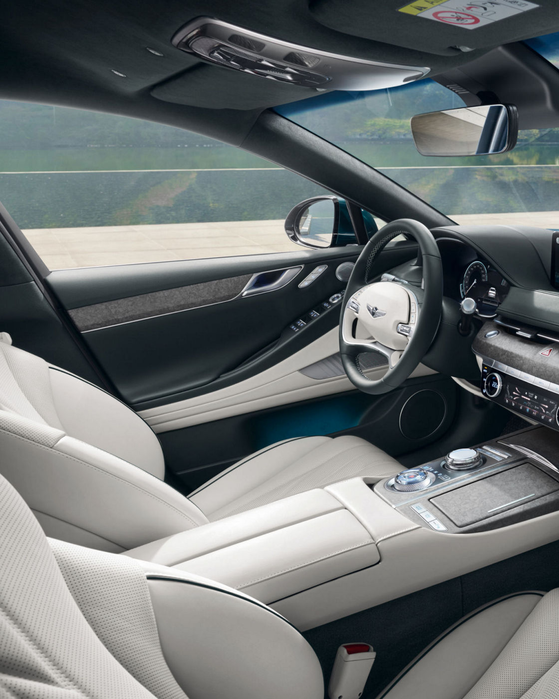 A luxury interior of the Electrified G80, featuring white perforated leather seats, a minimalistic dashboard, and a panoramic window view.