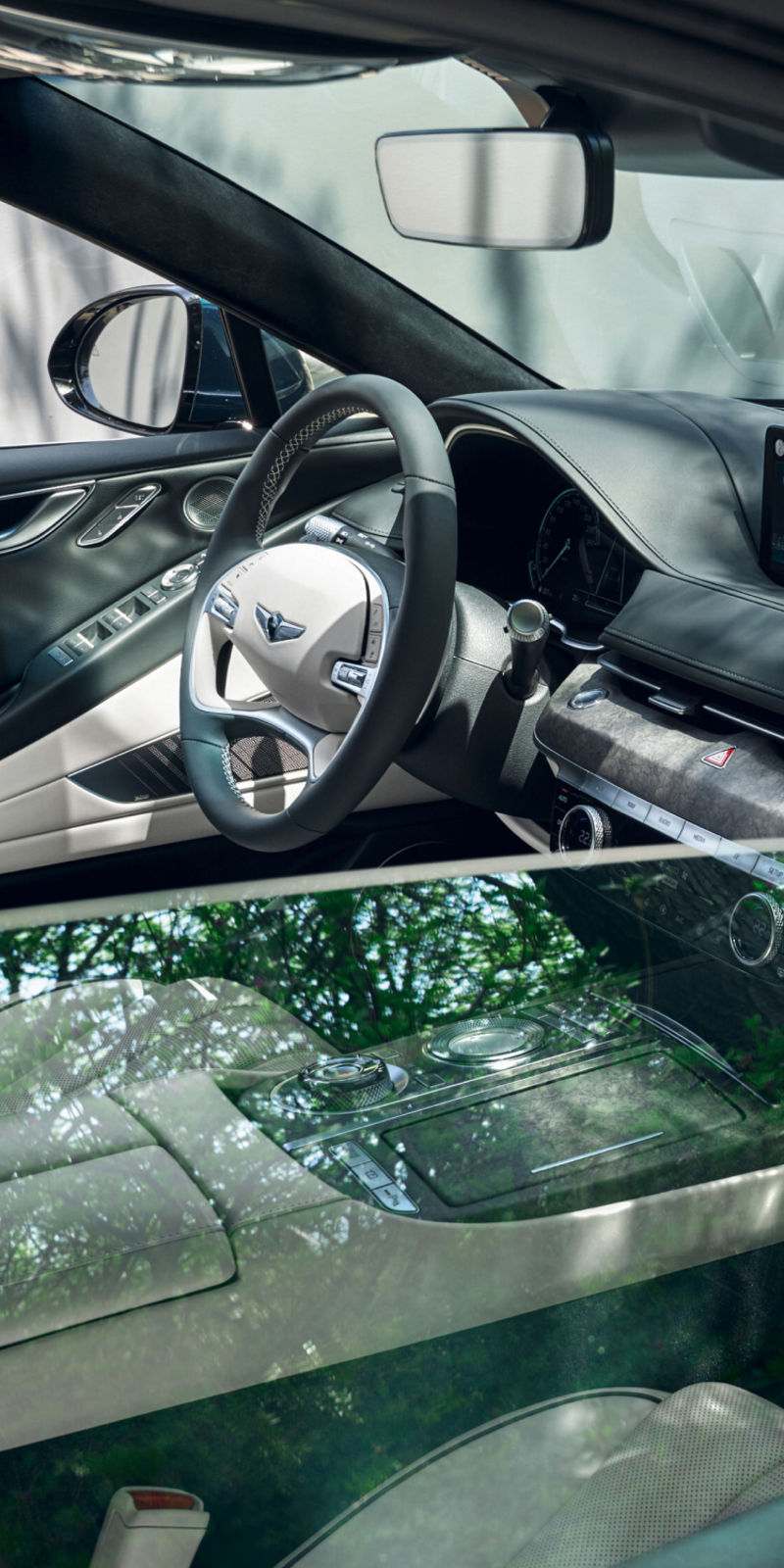 A partial view of the Electrified G80’s white interior seen through a reflective side window under natural lighting with green foliage.