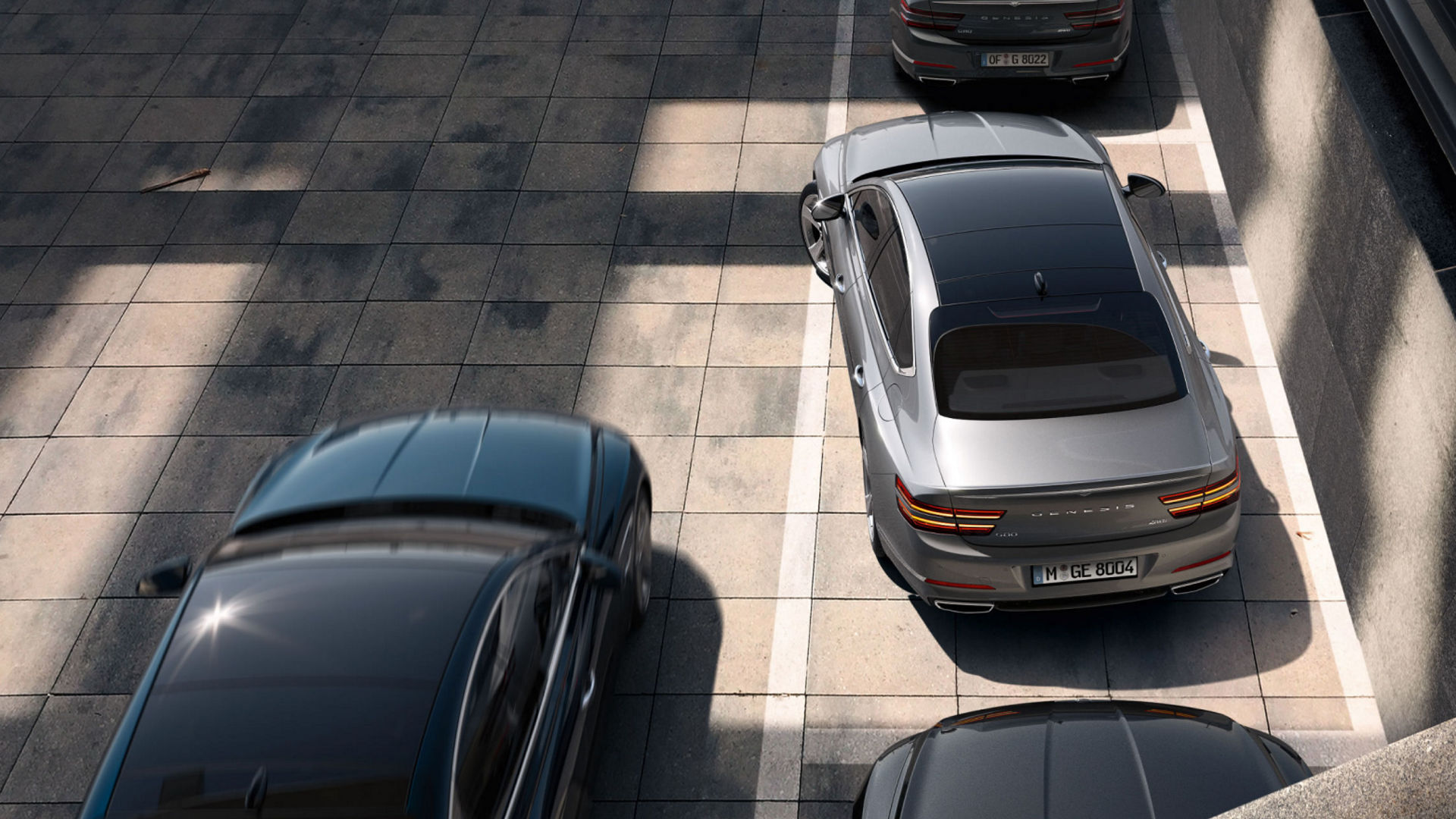 A silver Electrified G80 parked in a shaded urban lot, seen from a top-down view.