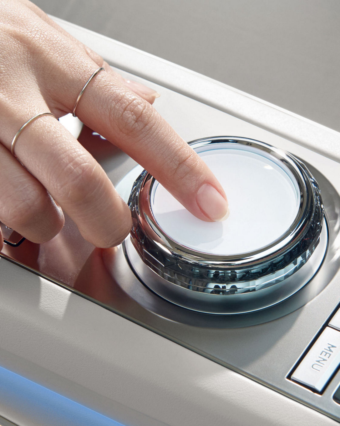 A close-up of a hand interacting with the rotary controller in the Electrified G80's interior.