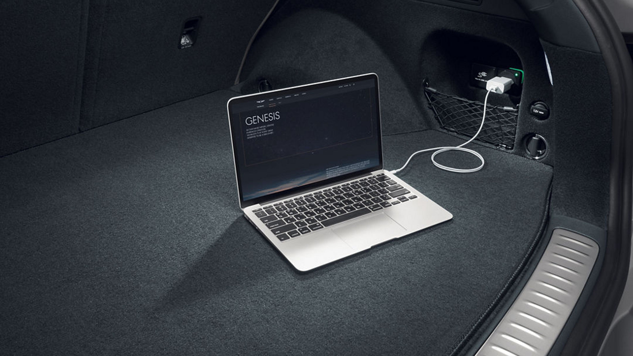 A laptop connected to a power outlet in the spacious cargo area of a Genesis vehicle, showcasing its practicality and convenience.