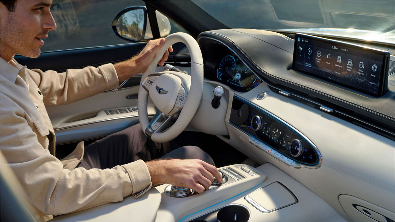 Ein Fahrer sitzt bequem in einem Genesis-Fahrzeug und interagiert mit dem Infotainmentsystem sowie den luxuriösen Innenraummaterialien