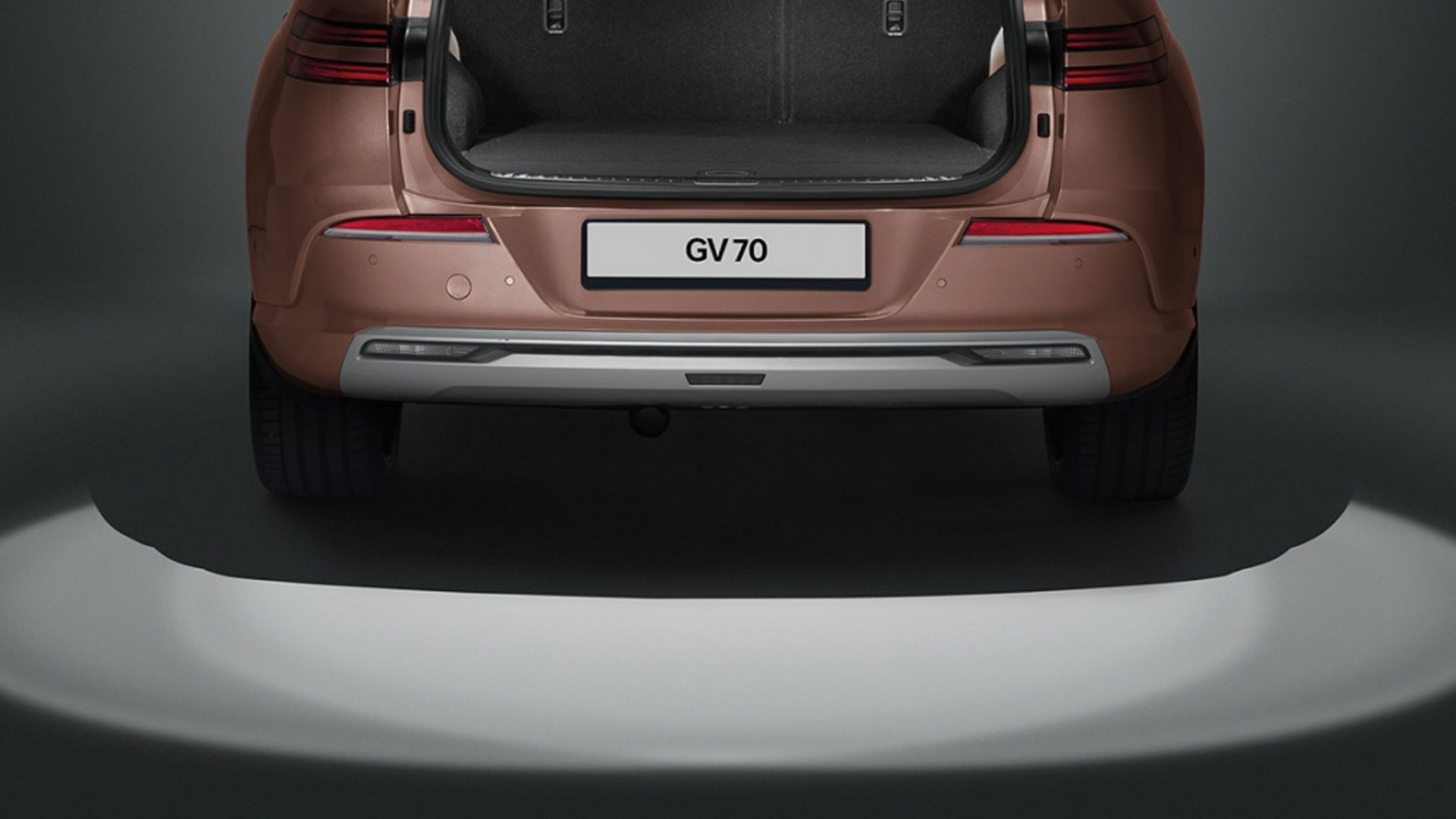 The rear view of an Electrified Genesis GV70 with its tailgate open, featuring illuminated ground projection for added convenience and visibility.