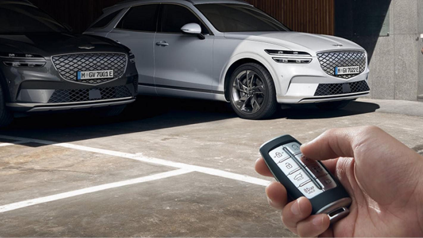 A hand holding a smart key fob activating the Electrified Genesis GV70's remote parking feature while parked in a garage.