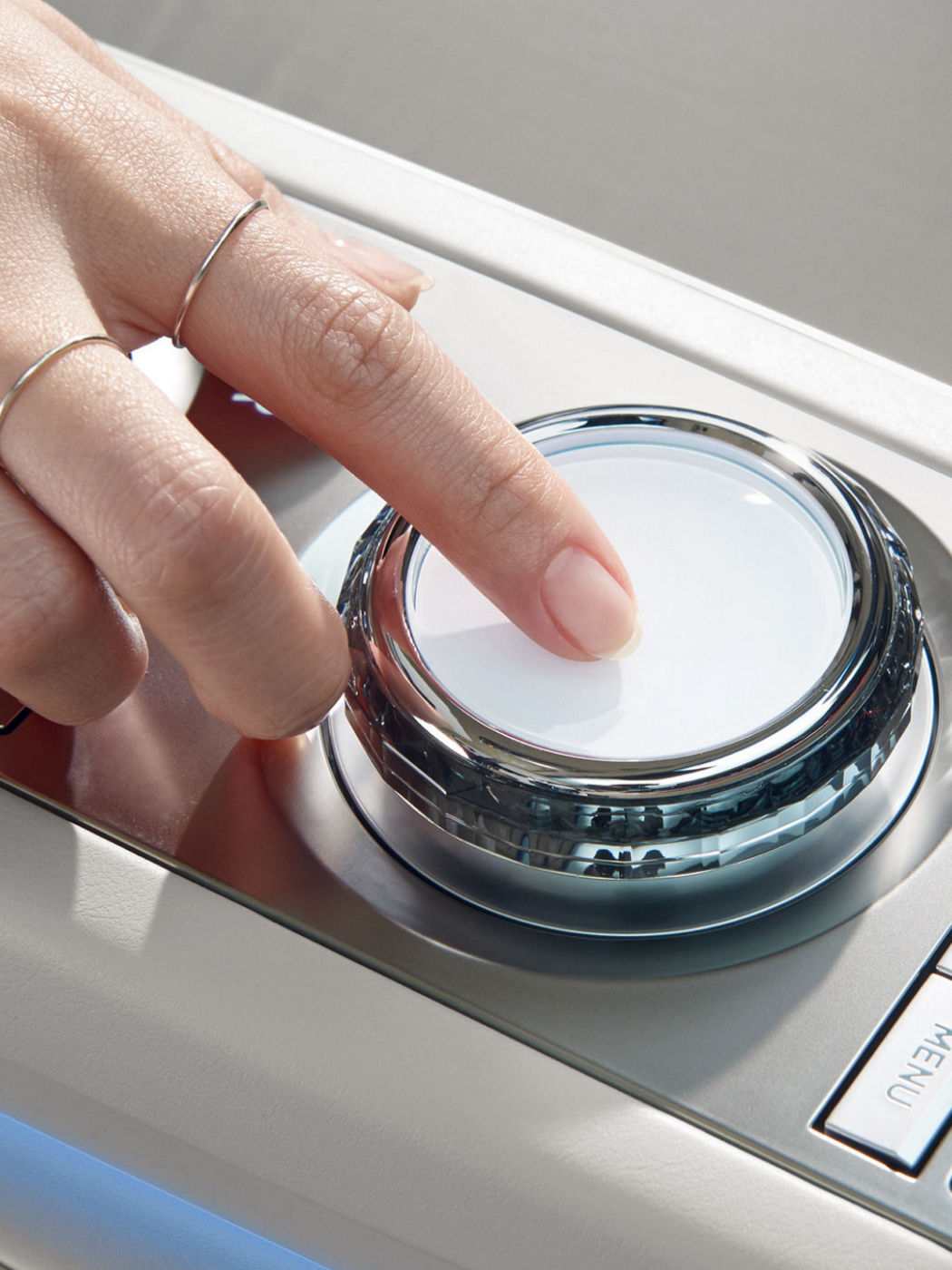 A close-up of a hand interacting with a glossy control dial in a Genesis vehicle's center console.