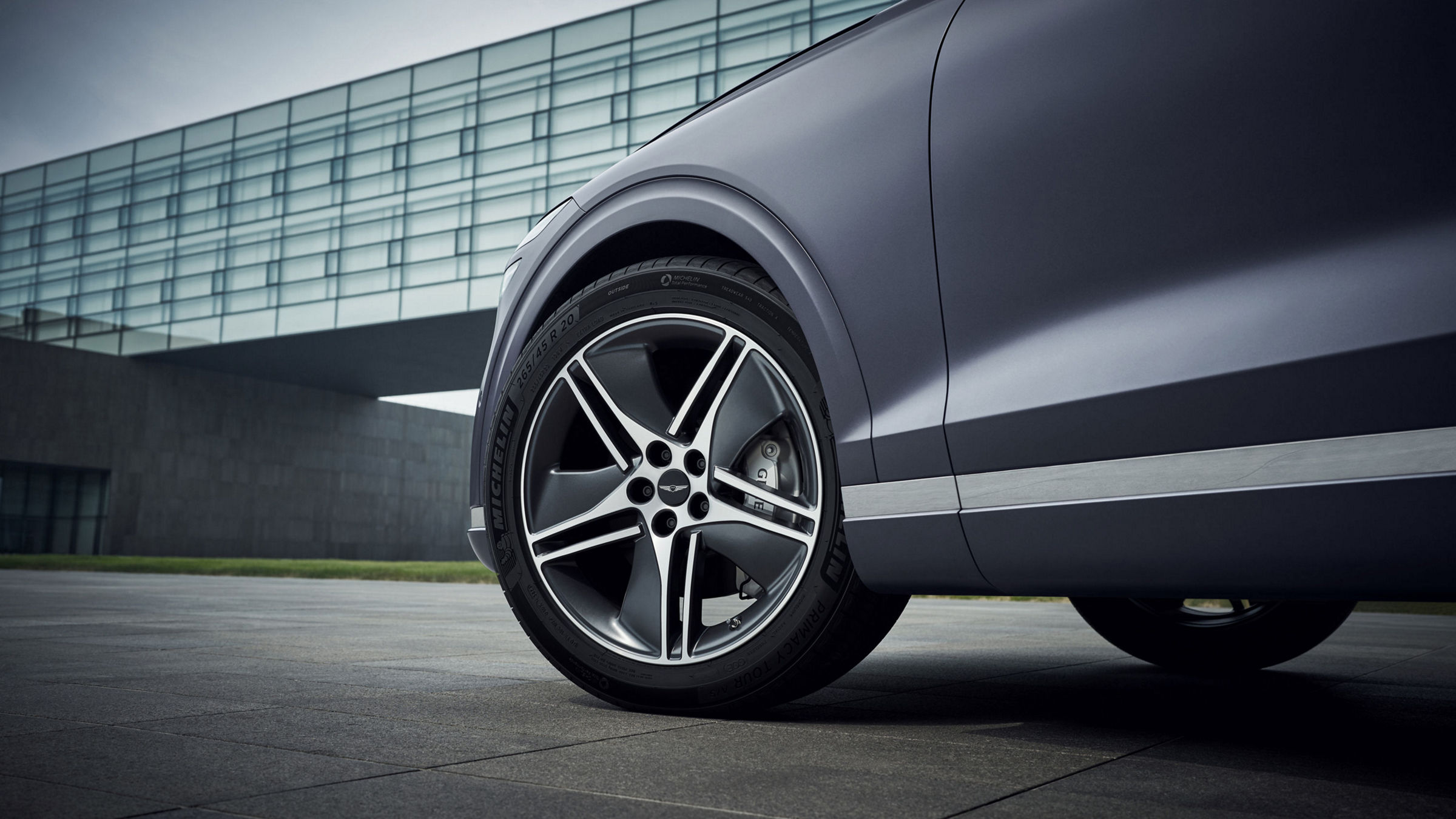 Het wiel van de Genesis Electrified GV70 draait naar links op een zwarte geasfalteerde weg.