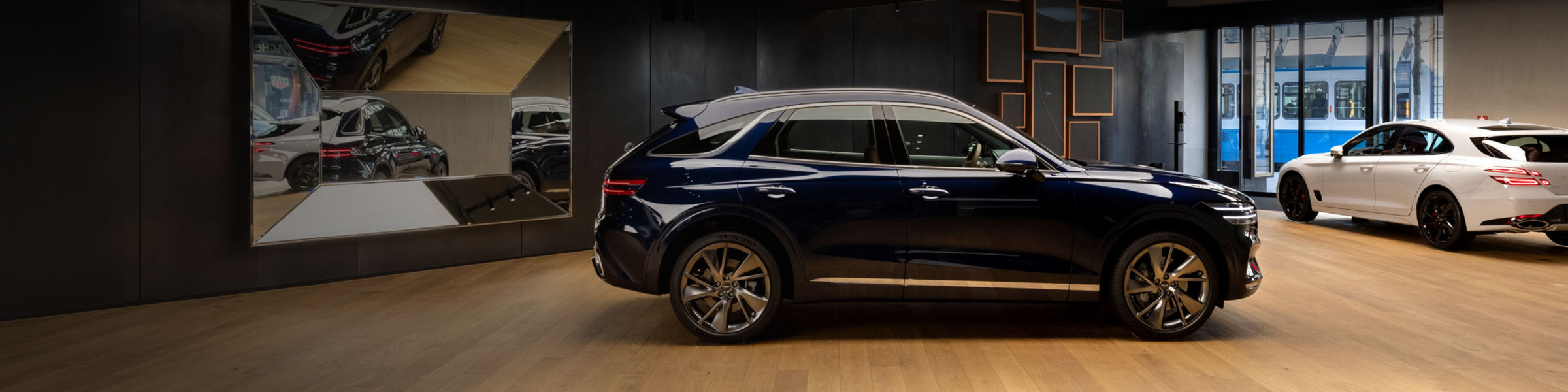 Showroom with a blue GV80 SUV and a white sedan on a wooden floor