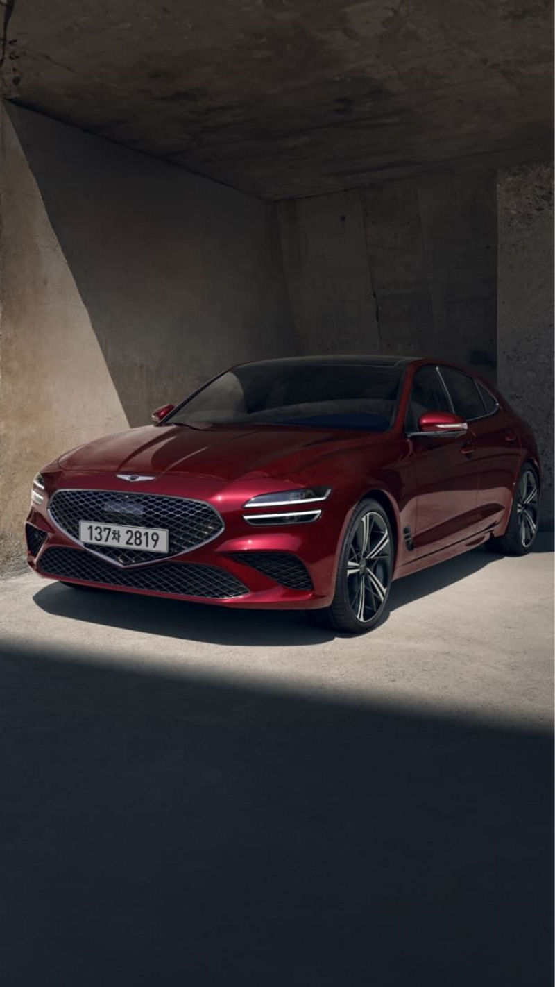 The G70 Shooting Brake in vibrant red, parked under soft sunlight, highlighting its bold front grille and sharp headlights.