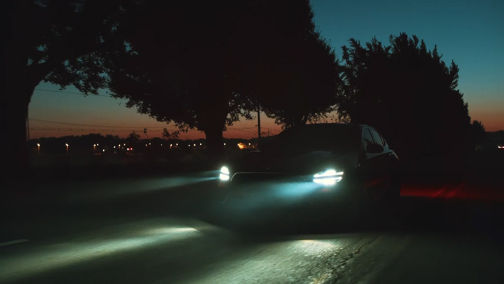 A Genesis G70 driving at night with headlights illuminating the road ahead.