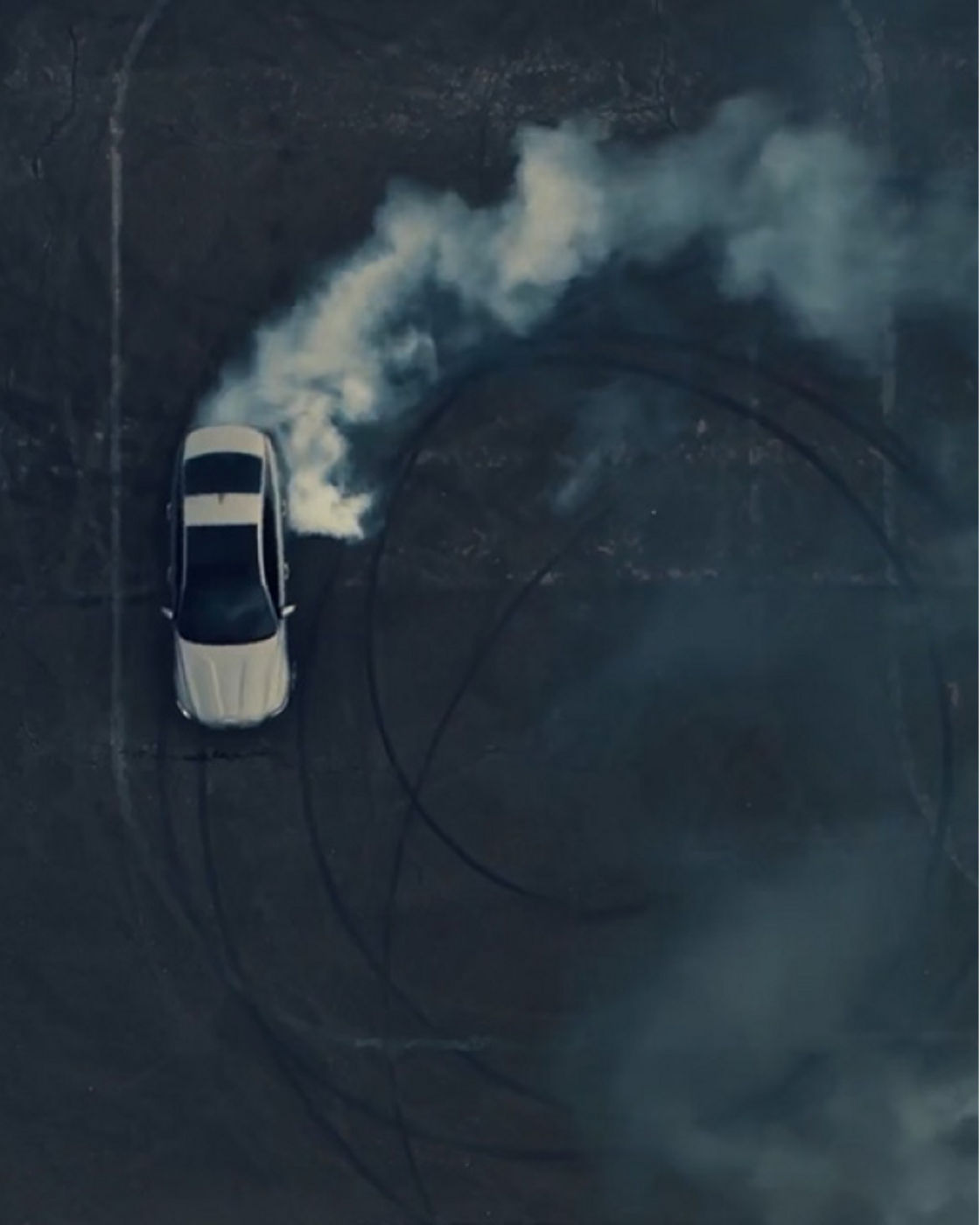 A top-down view of a Genesis G70 performing a drift with smoke trails.