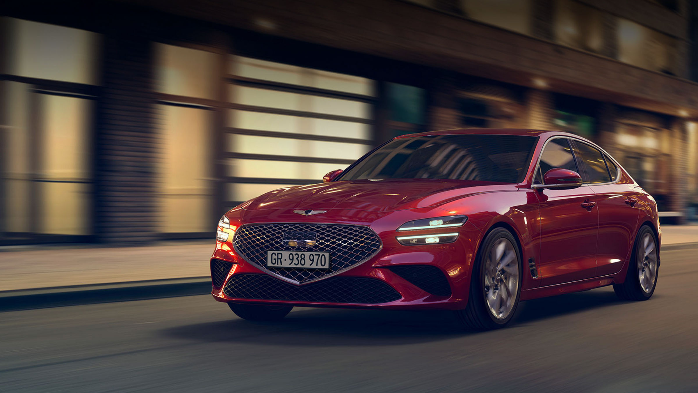 A red Genesis G70 driving through a city street at night.