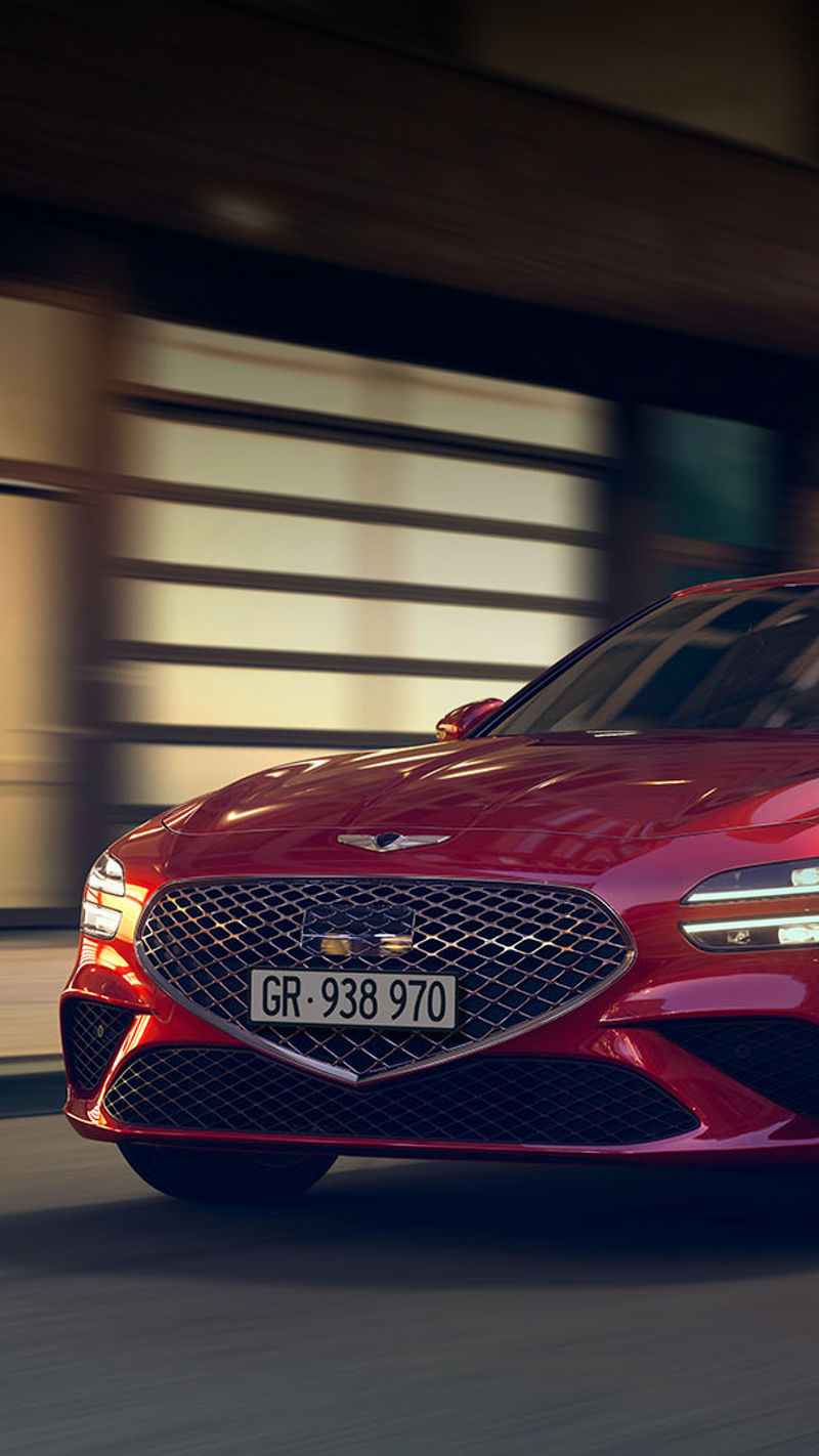 A red Genesis G70 driving through a city street at night.