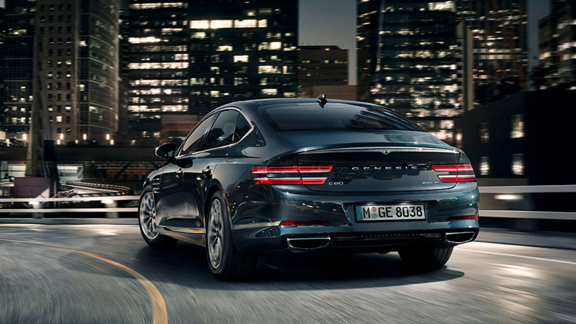 A rear view of the G80 driving through city streets at night, showcasing its sleek taillights and commanding presence.