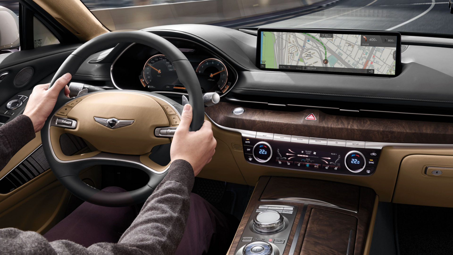 Driver's view of the Genesis G80 interior, featuring a navigation display, beige and wood accents, and smart cruise control.