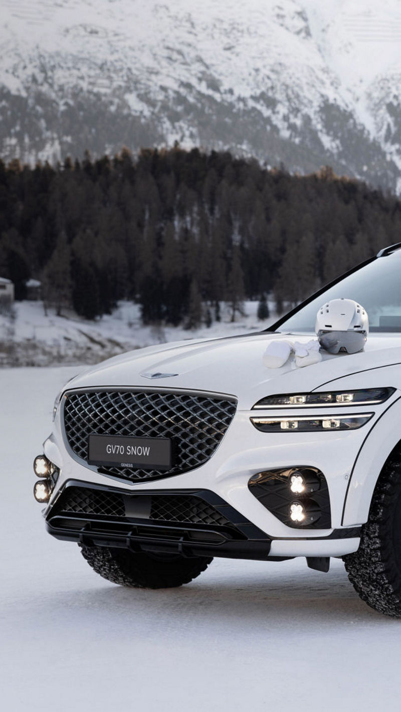 White Genesis GV70 Snow concept on snow with ski equipment in front of snow-covered mountain