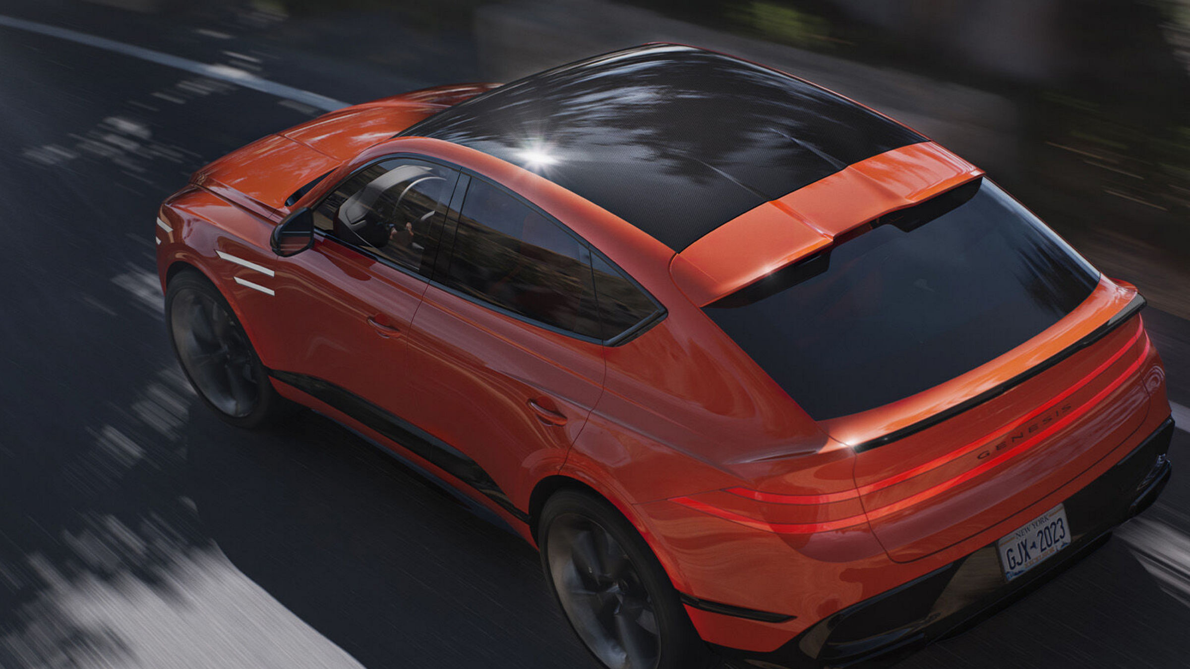 Rear view of the Genesis GV80 Coupe in orange, driving on a road with reflections on the roof