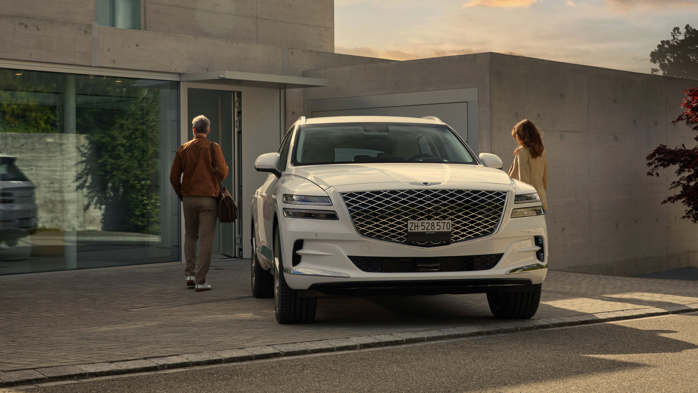 White Genesis GV80 in front of a house with two people next to it.