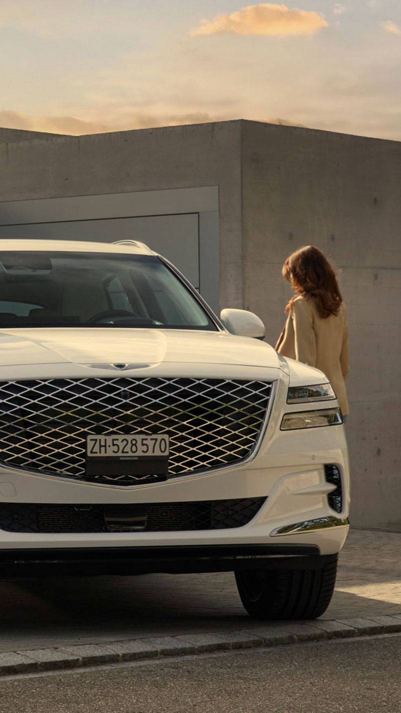 White Genesis GV80 in front of a house with two people next to it.