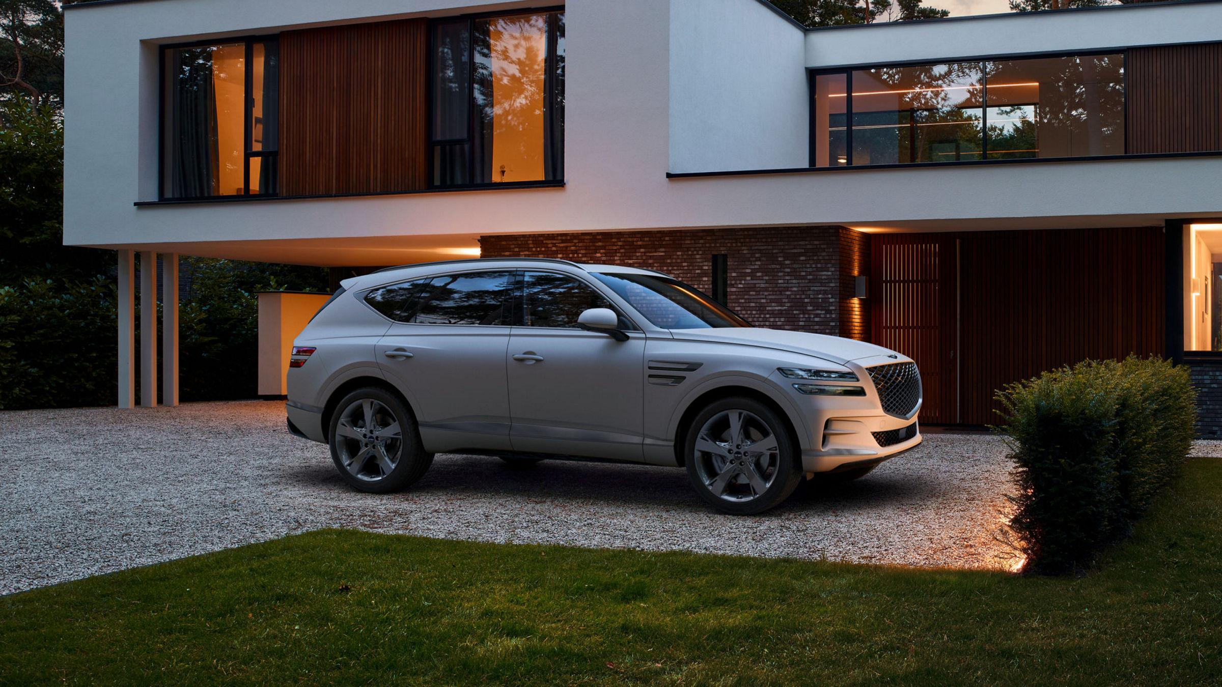 White Genesis GV80 next to a meadow in front of a modern building with several people inside