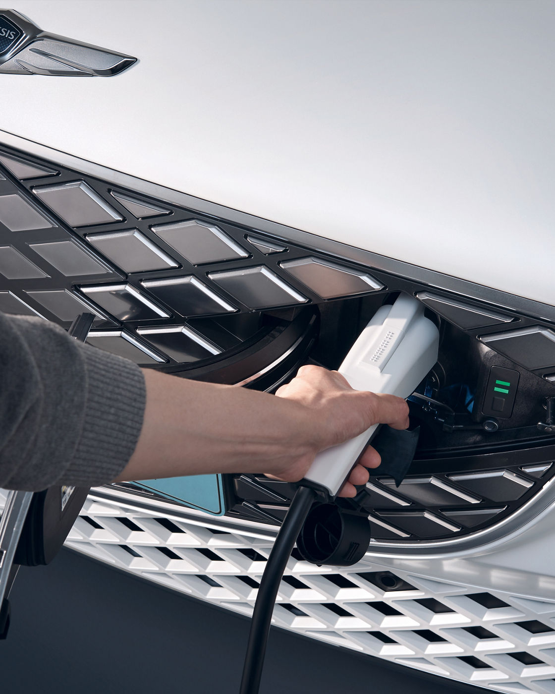 An arm plugs a charging cable into the charging port of a white car