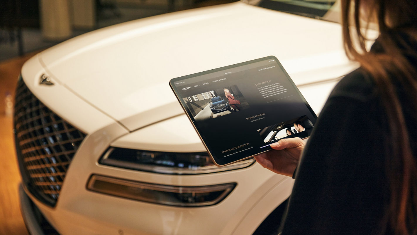 Woman with an Ipad in her hand in front of the front part of the Genesis GV70