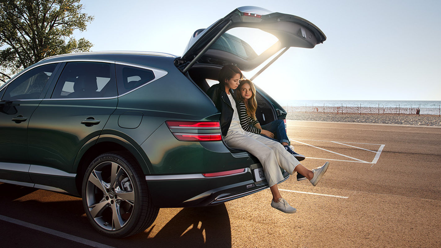 Green Genesis GV80 in the sunset on the road with two people in the open boot