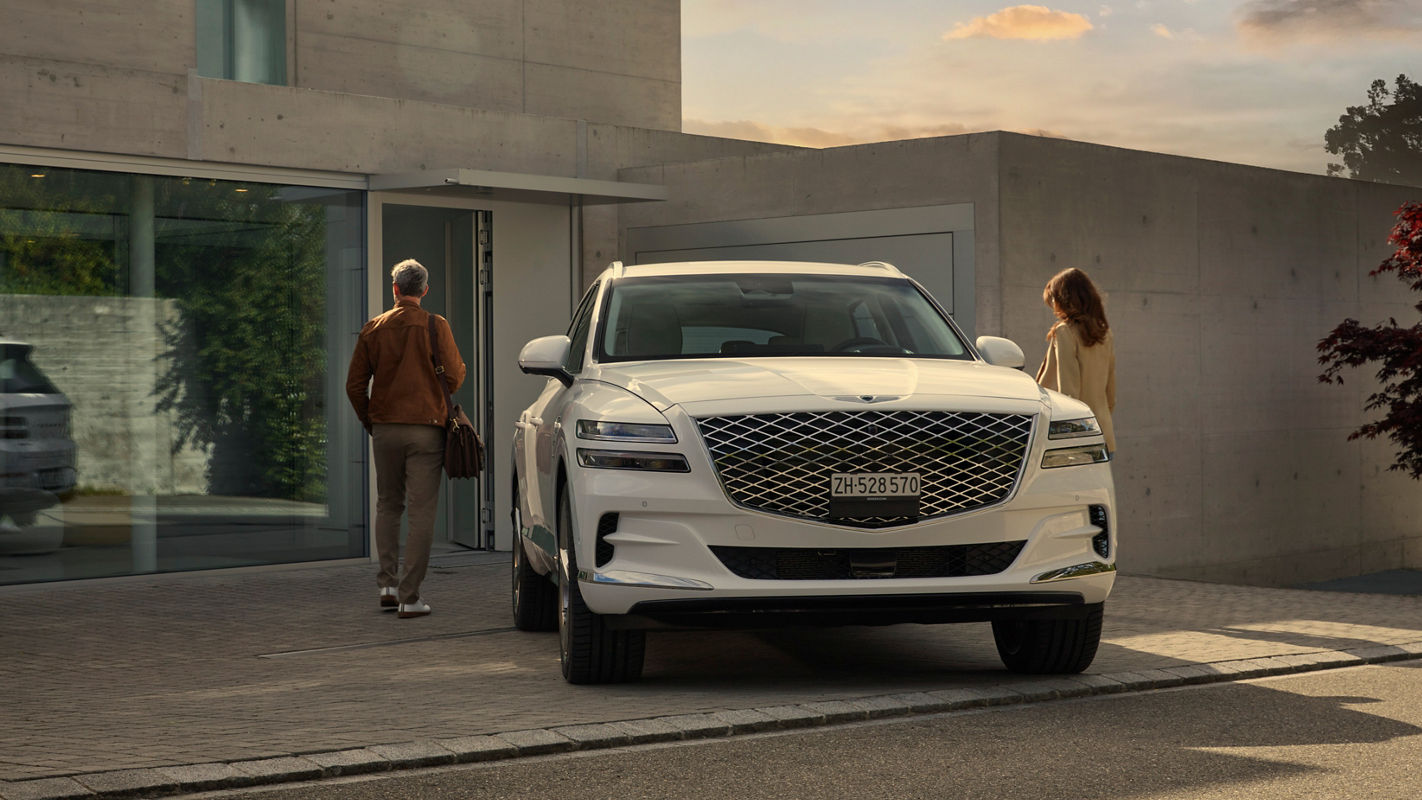 White Genesis GV80 in front of a house with two people next to it