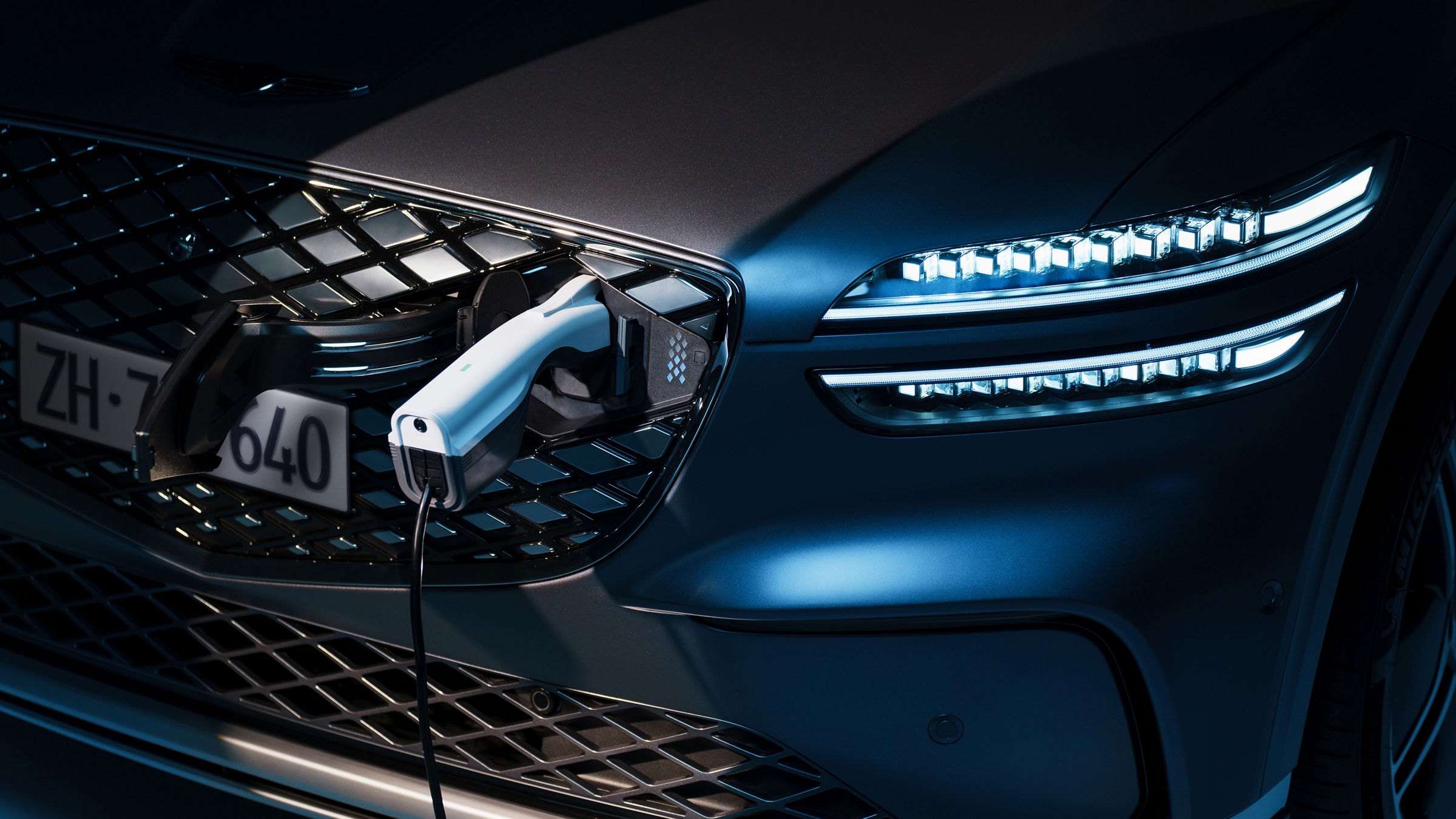 A close-up view of the Genesis Electrified GV70's charging port, integrated into the vehicle's front grille.