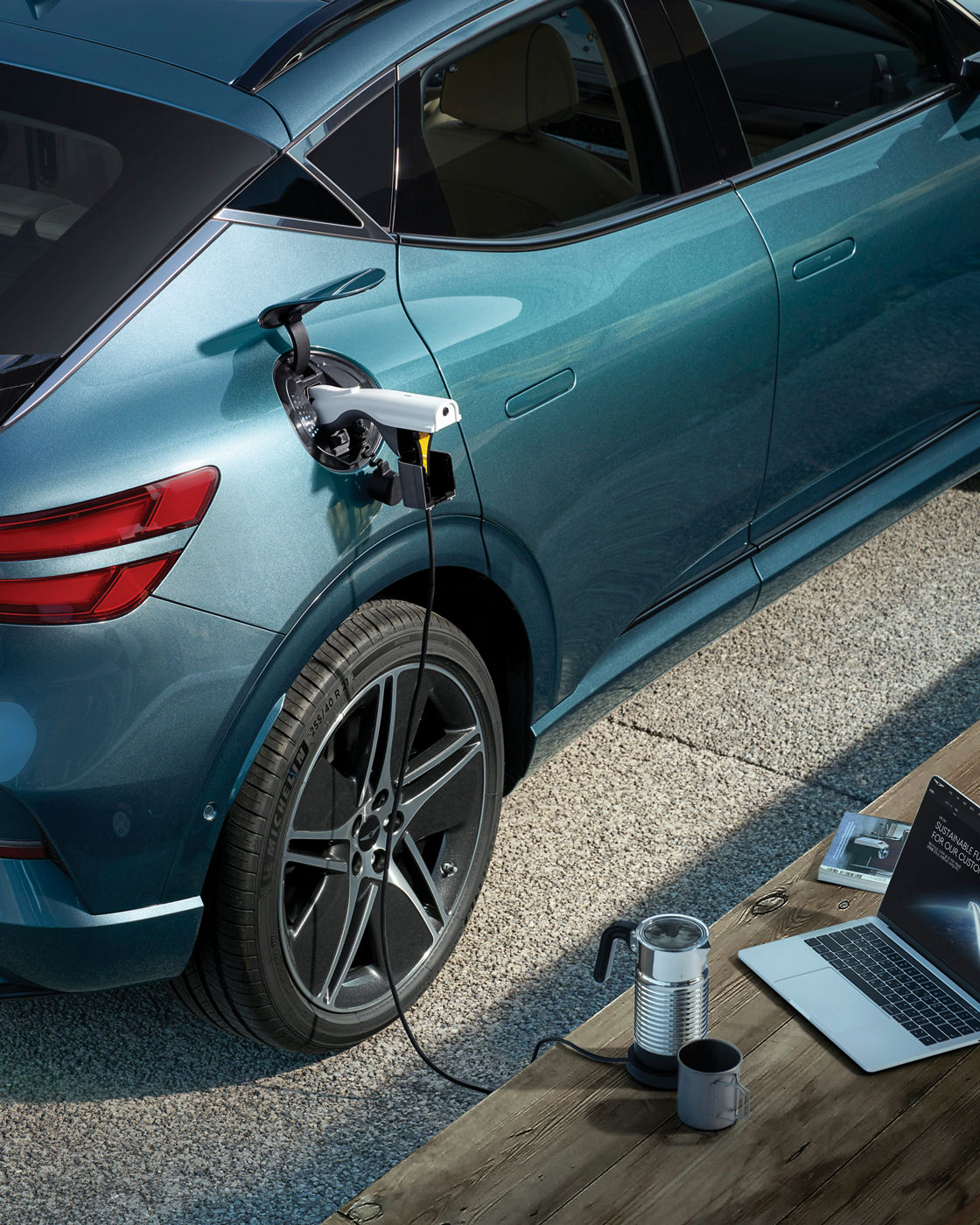 A gender connector connected to the front charging port of the Genesis EV vehicle is connected to the laptop located in front of the vehicle.