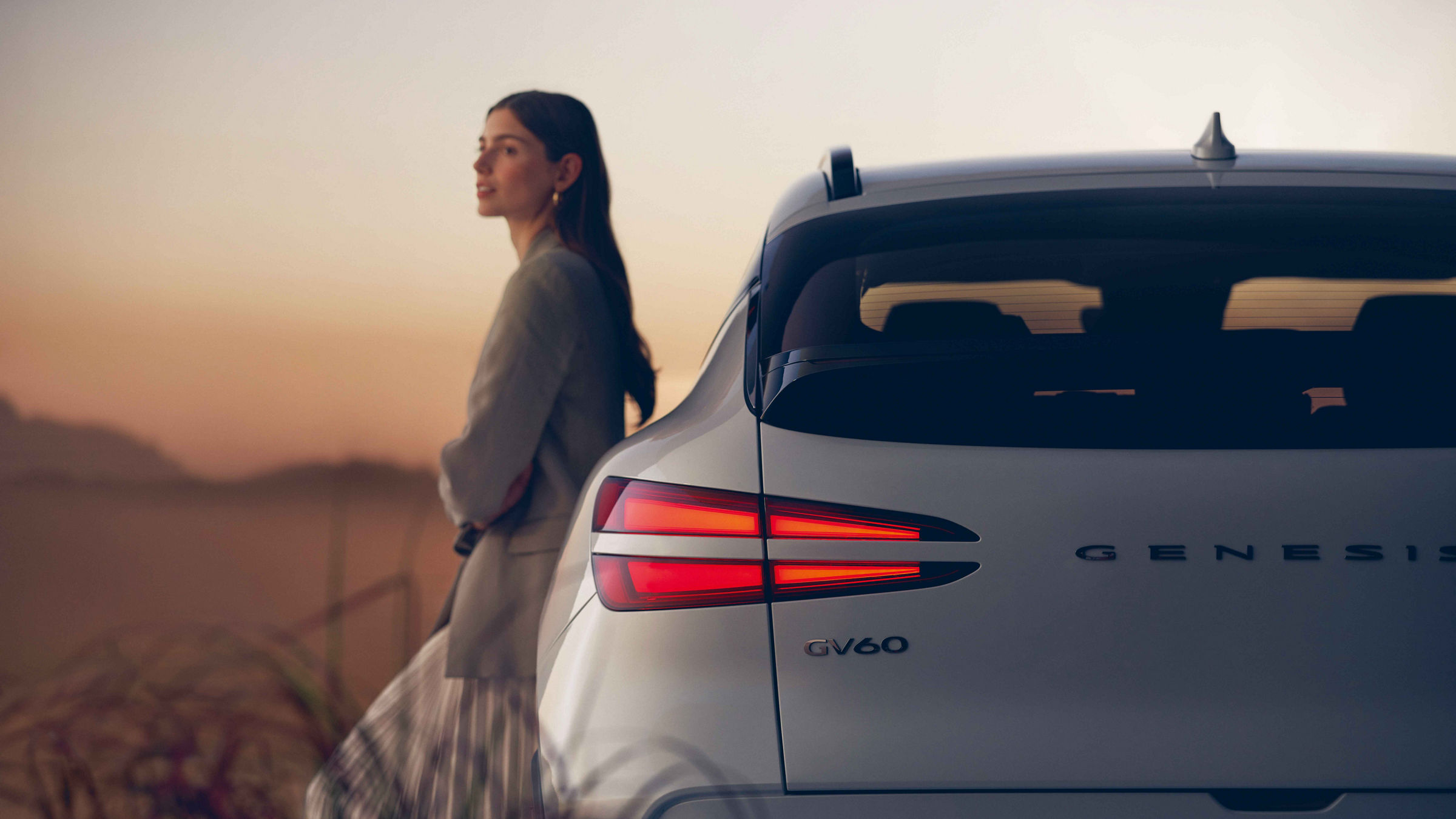 Woman leaning against a Genesis GV60 and looking into the distance