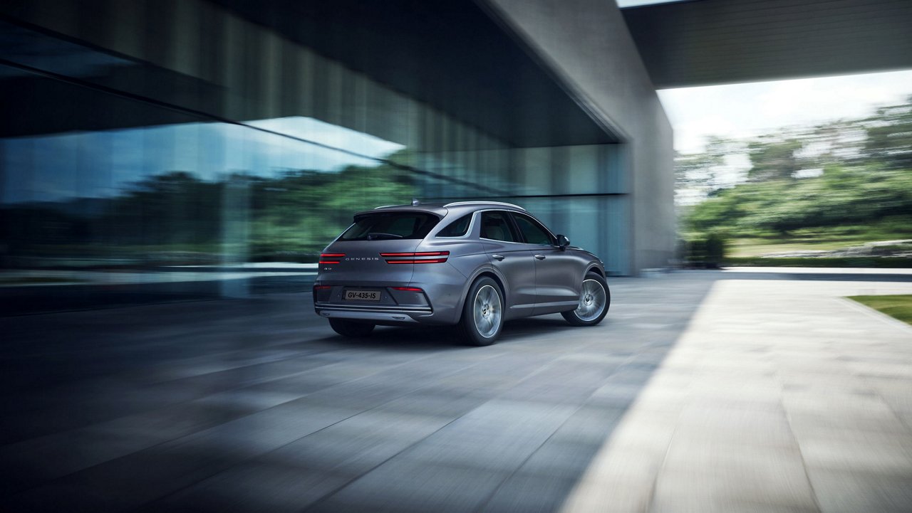 The Electrified GV70 drives along a road surrounded by buildings.