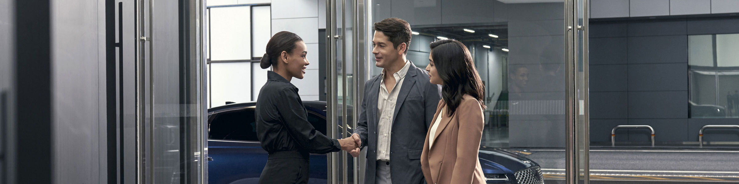 People greeted by Personal Assistant in a Genesis Studio with a blue G80 outside