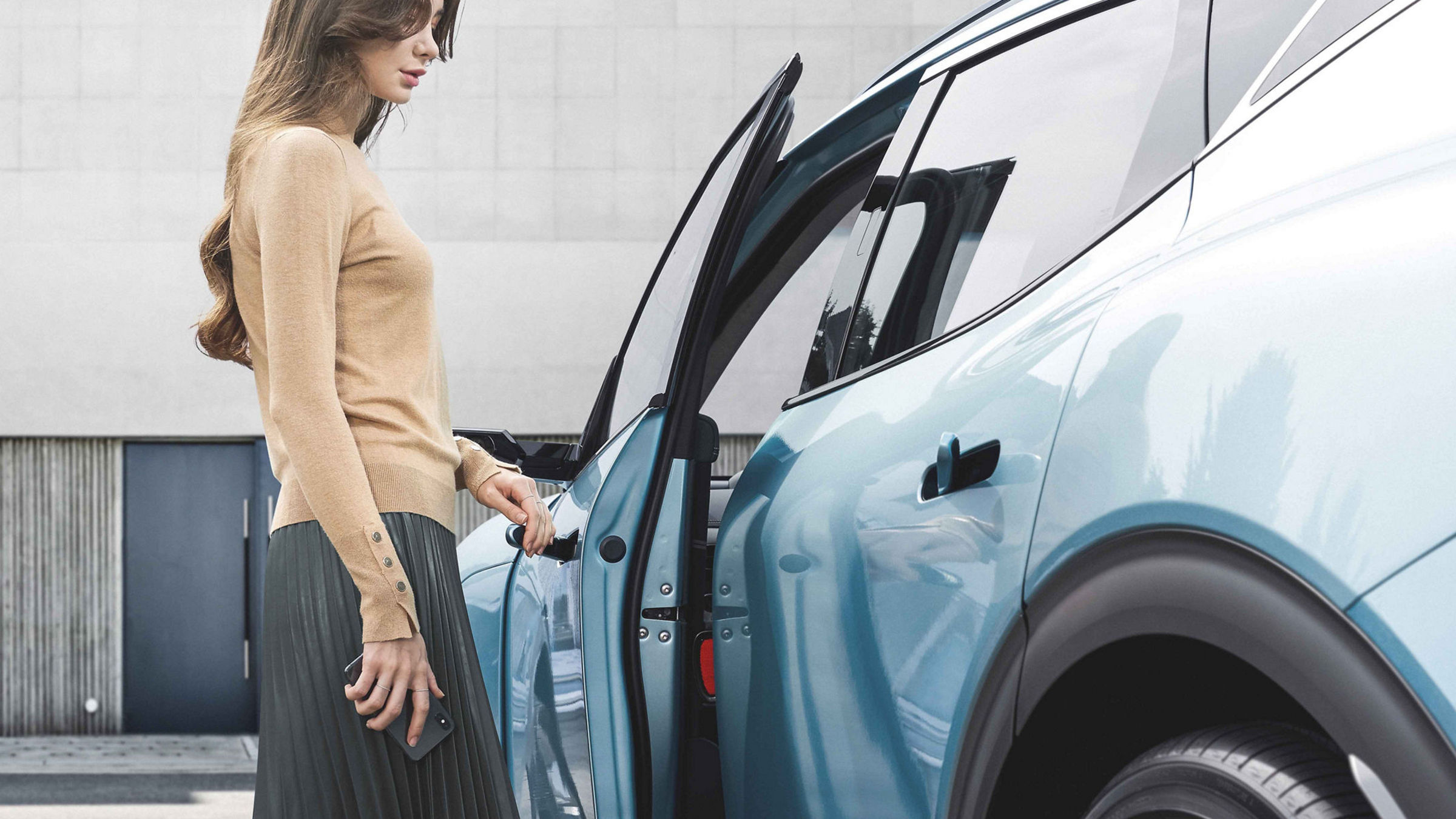 An arm plugs a charging cable into the charging port of a white car