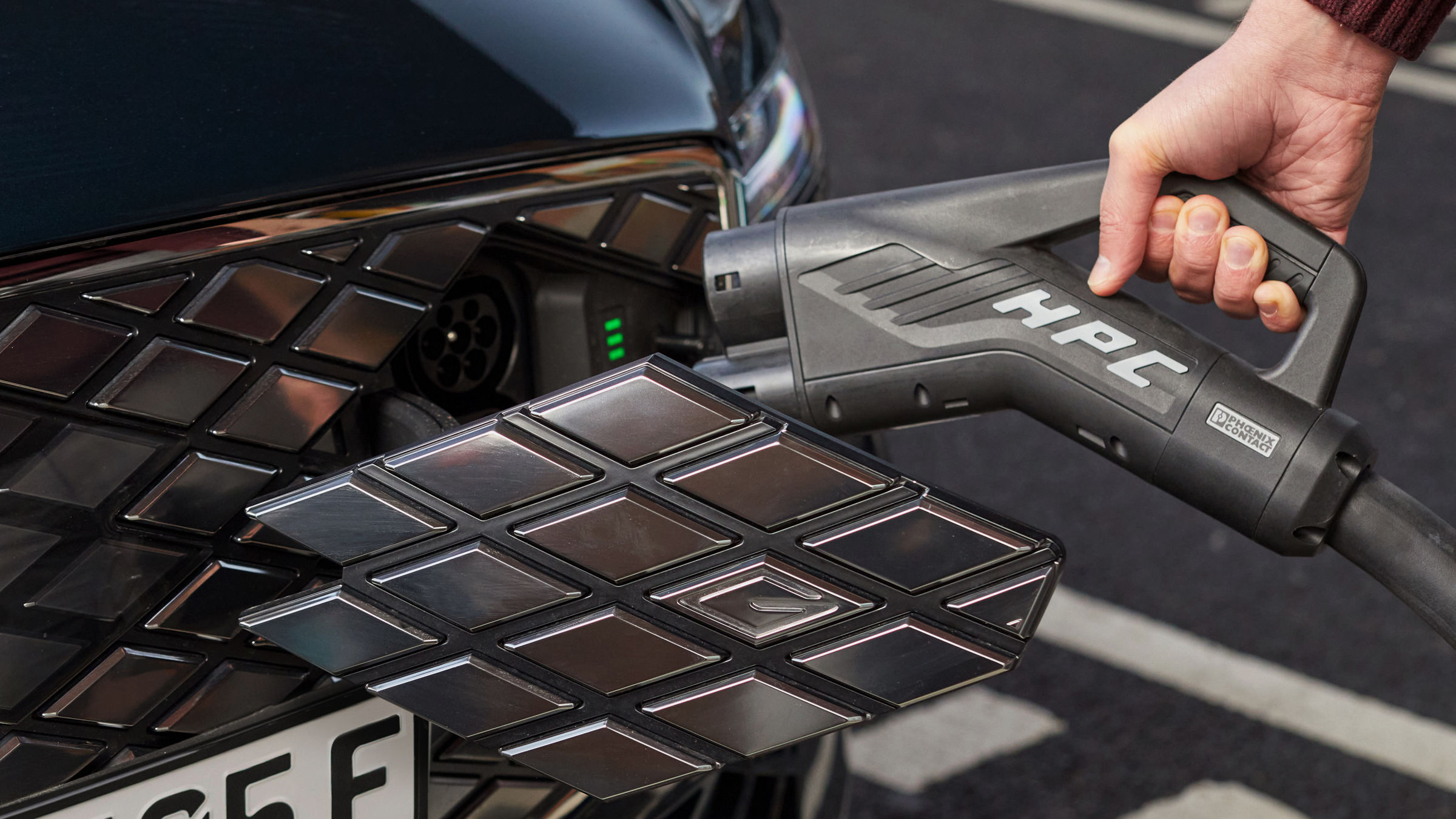 A hand plugs a charging cable into an electric car