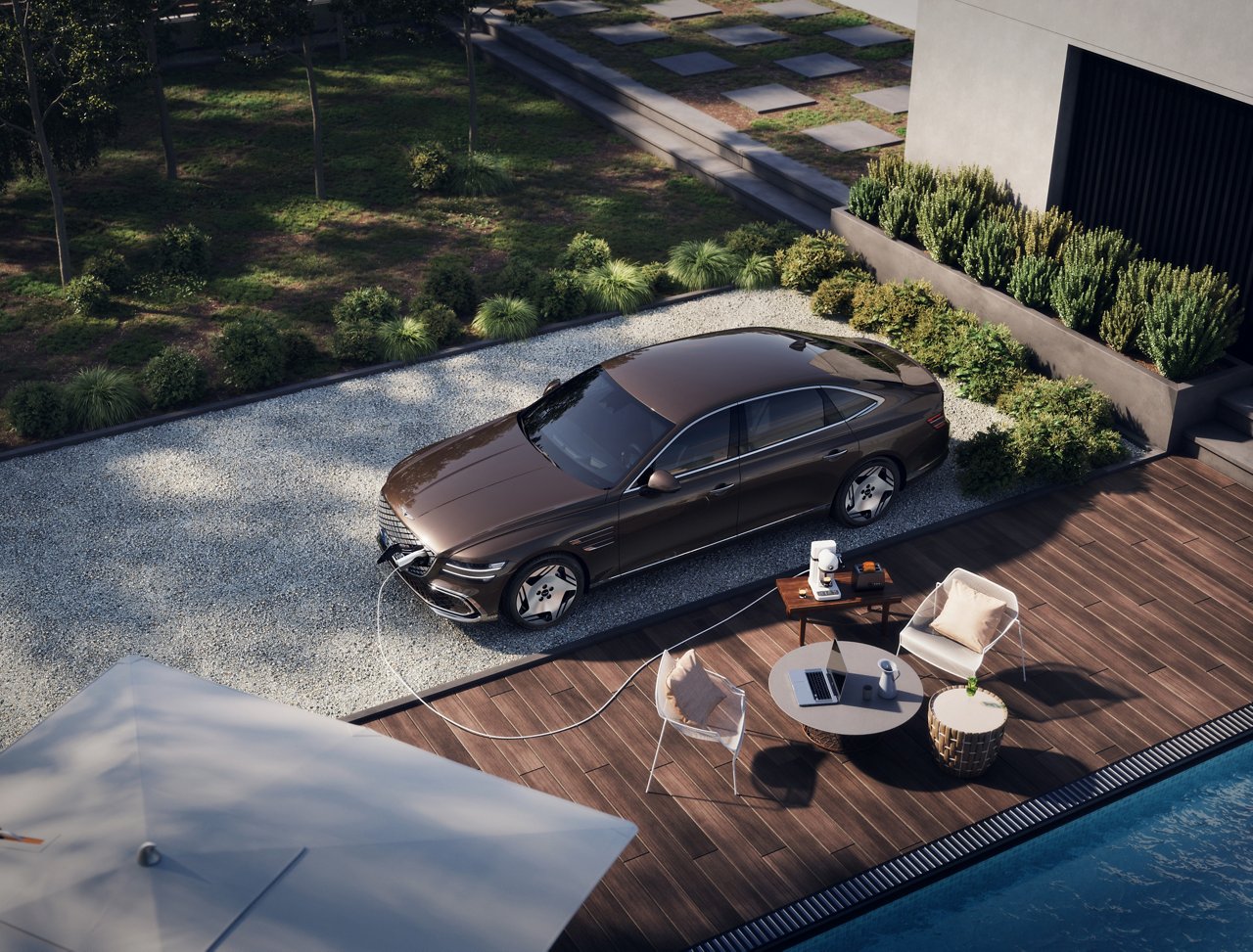 Electrified G80 is charging in a graveled garden area. A laptop on a coffee table, a small coffee machine, and more are visible in front of the car, creating a relaxed atmosphere.