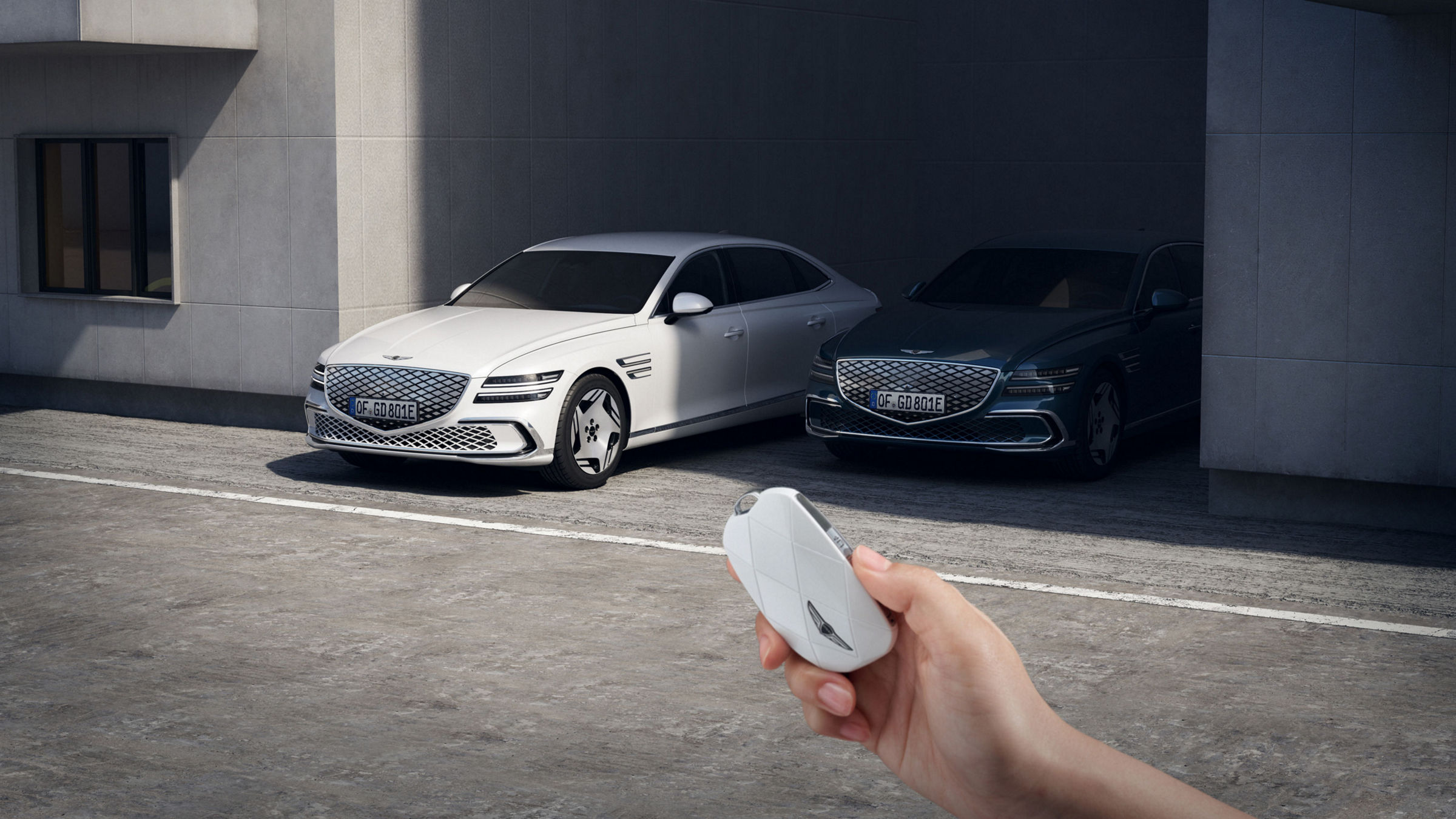 An electrified G80 is moving forward, leaving a shaded parking space, and in front of it you see a hand grasping the car keys.