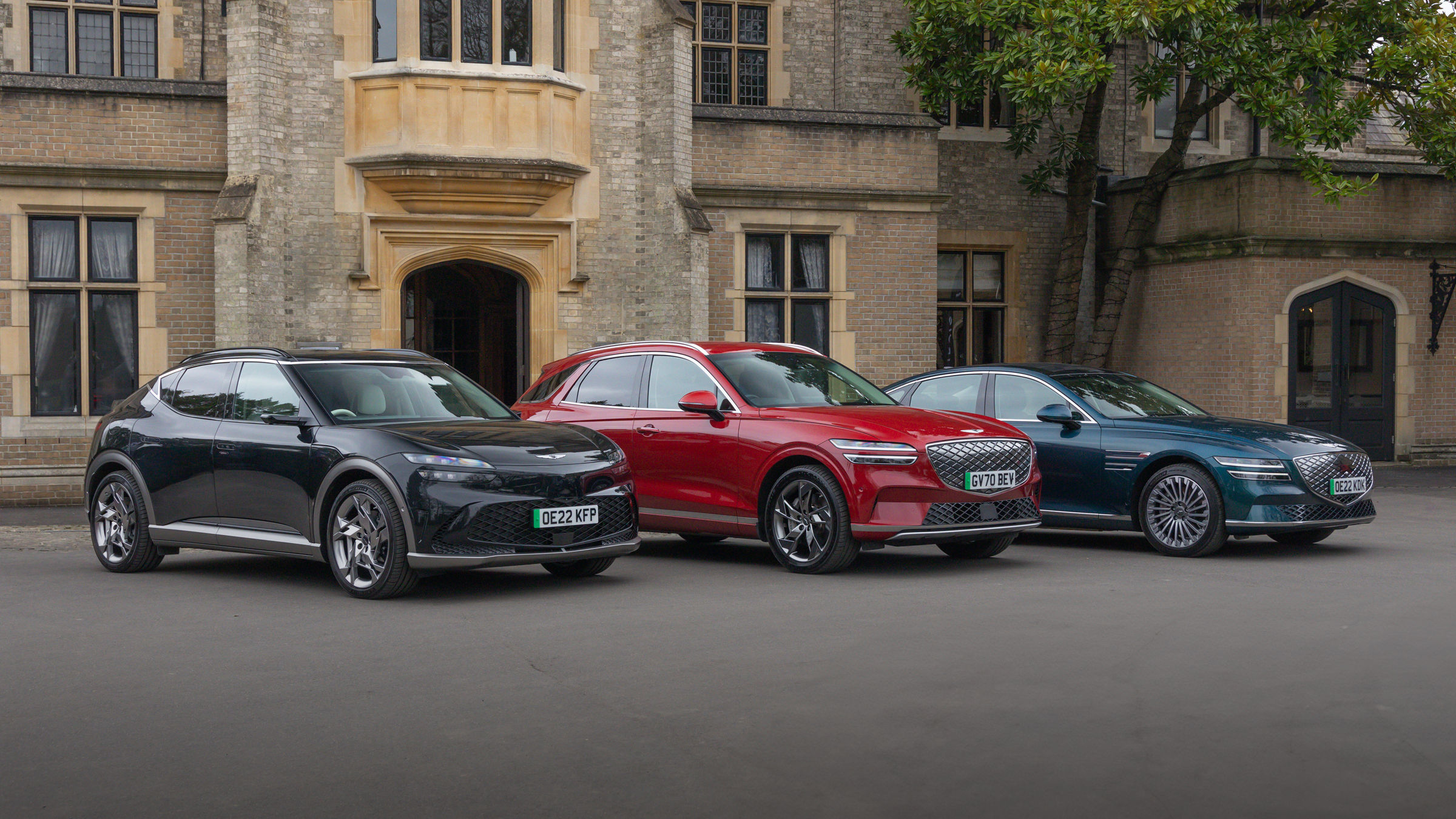 Three Genesis cars in black, red and blue in front of a building