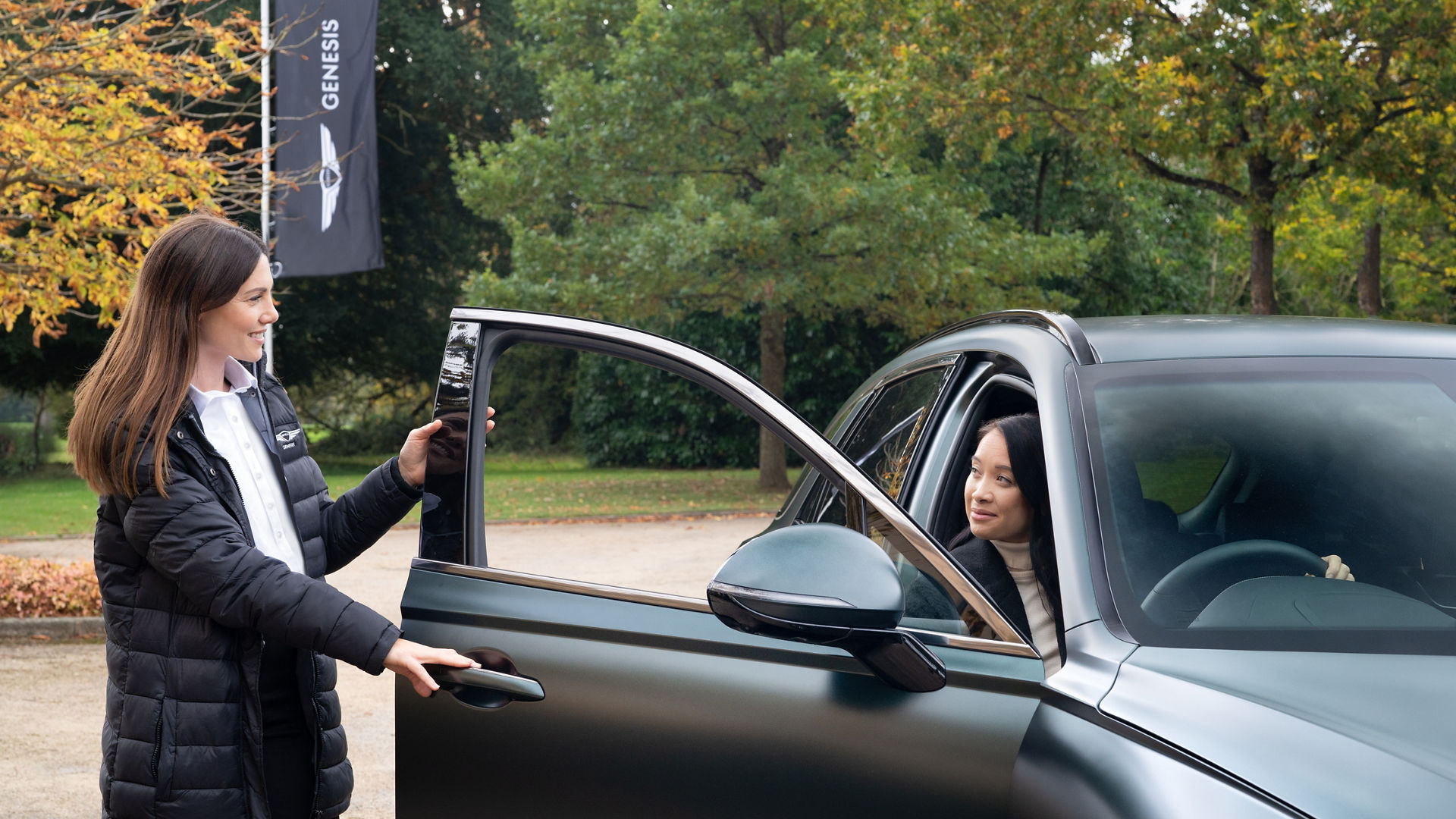 Woman standing at the open door of a car with another woman in the driver's seat