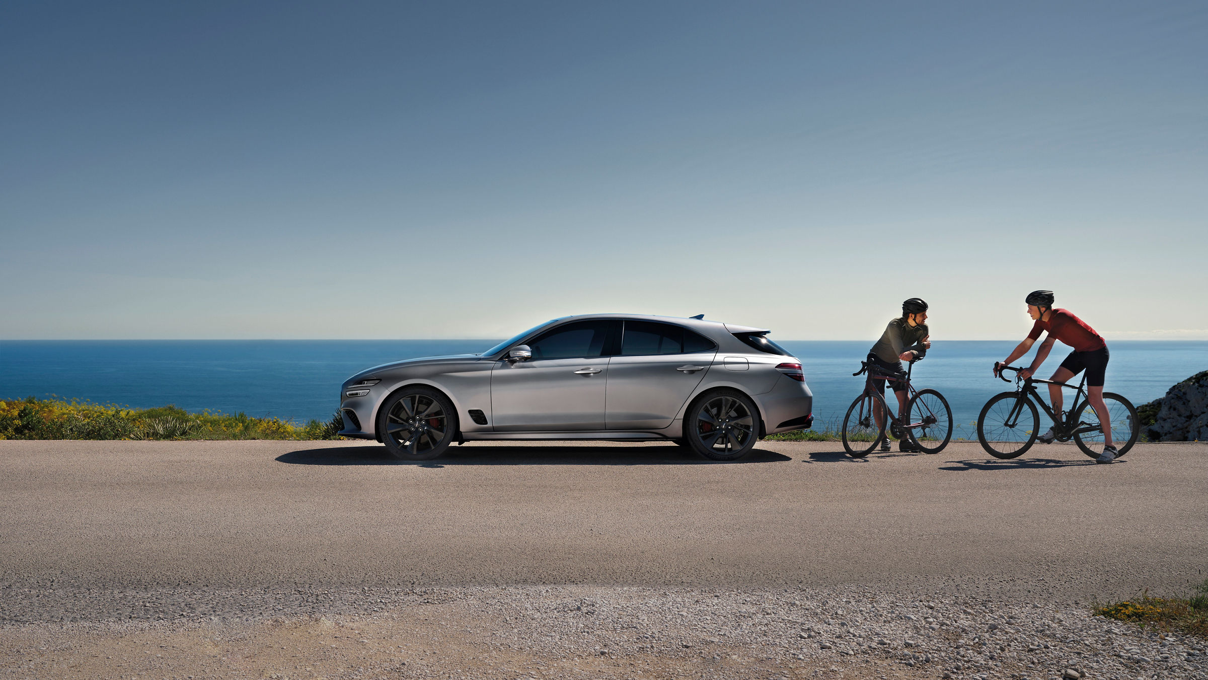 Genesis G70 Shooting Brake silver outdoor - side view in front of ocean with two cyclist