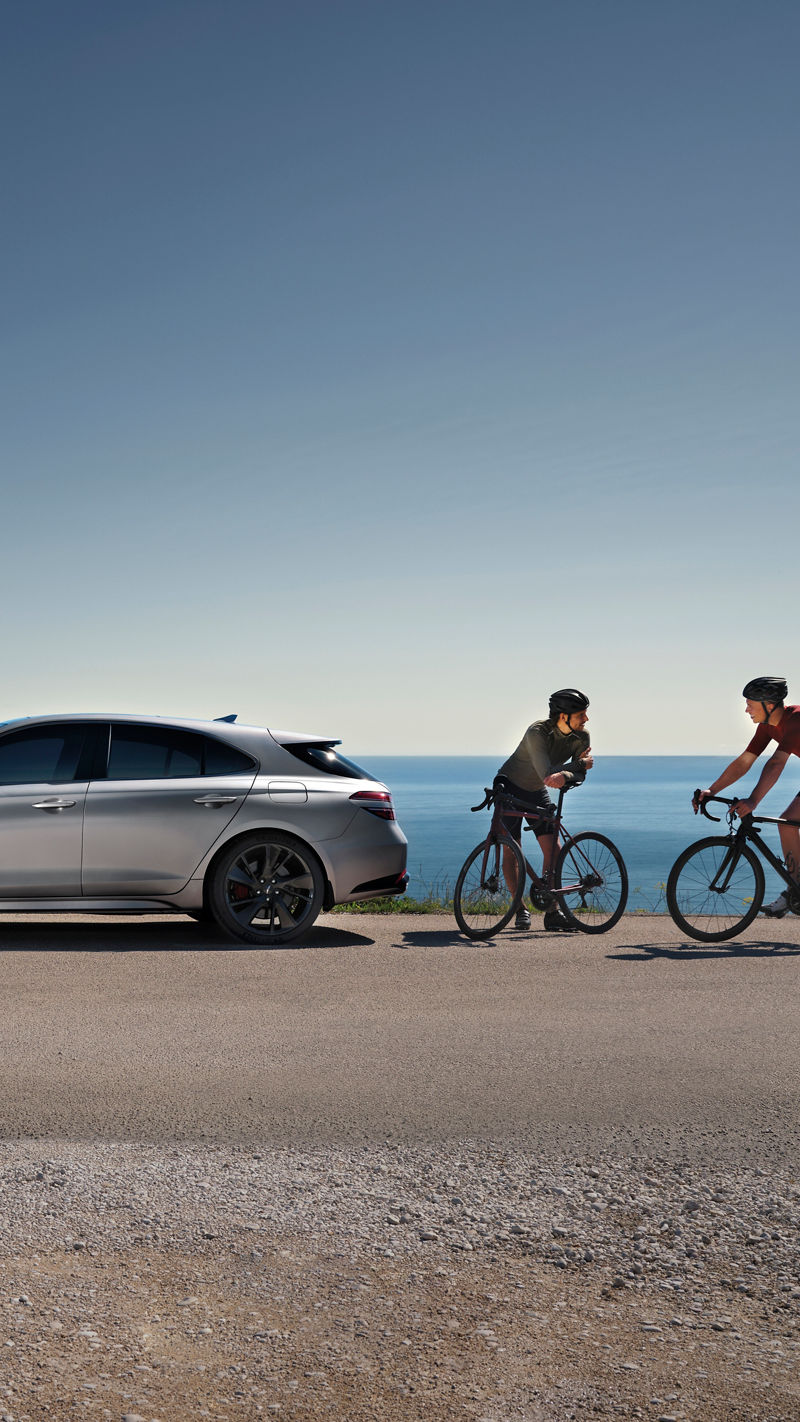 Genesis G70 Shooting Brake silver outdoor - side view in front of ocean with two cyclist