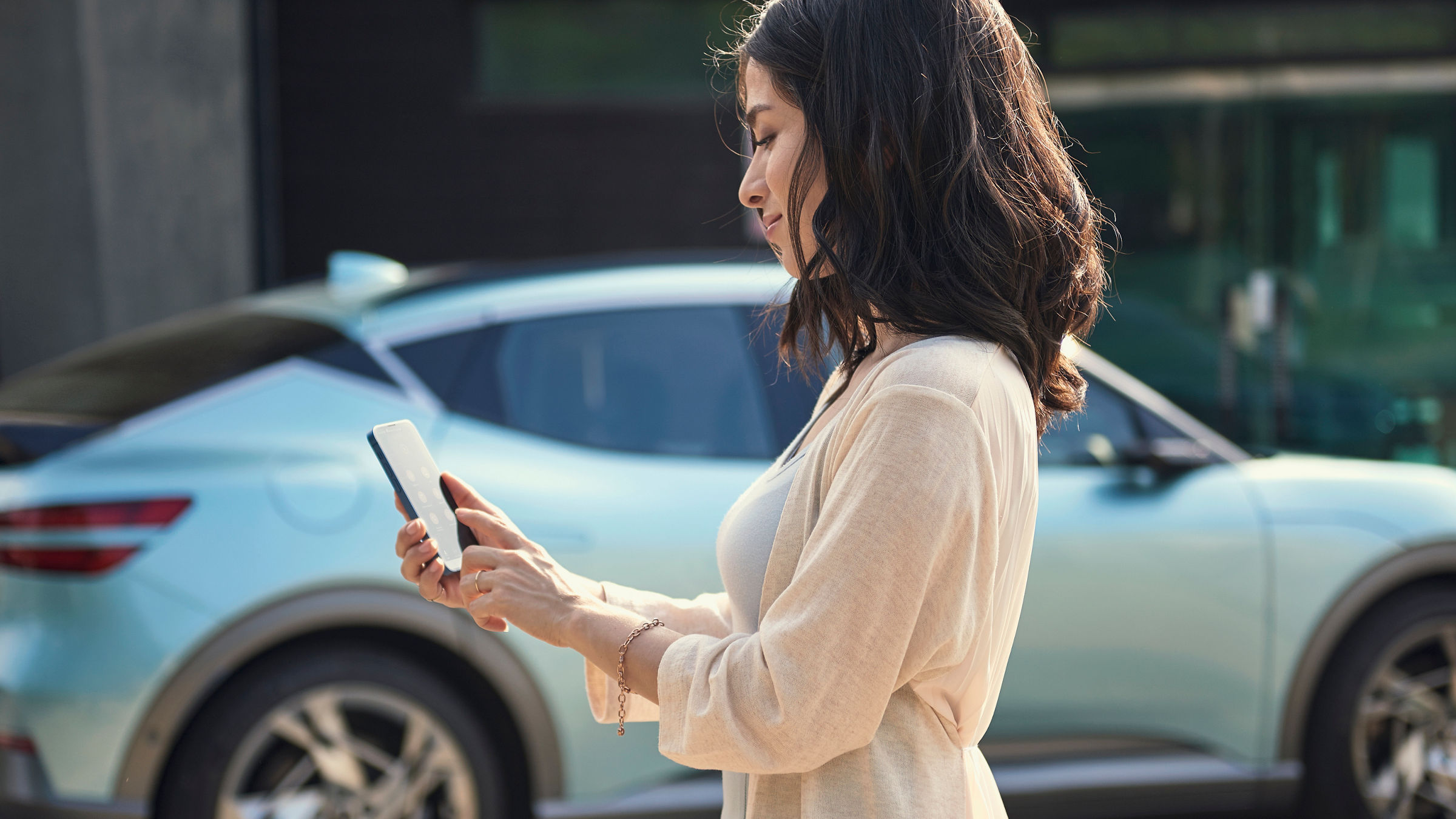 A woman uses her smartphone - in the background a mint-coloured Genesis GV60